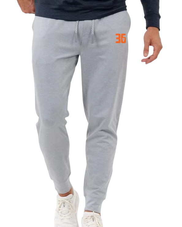 Close-up of a person wearing gray sweatpants and white sneakers, with a black long-sleeve shirt, standing with one hand near their side.