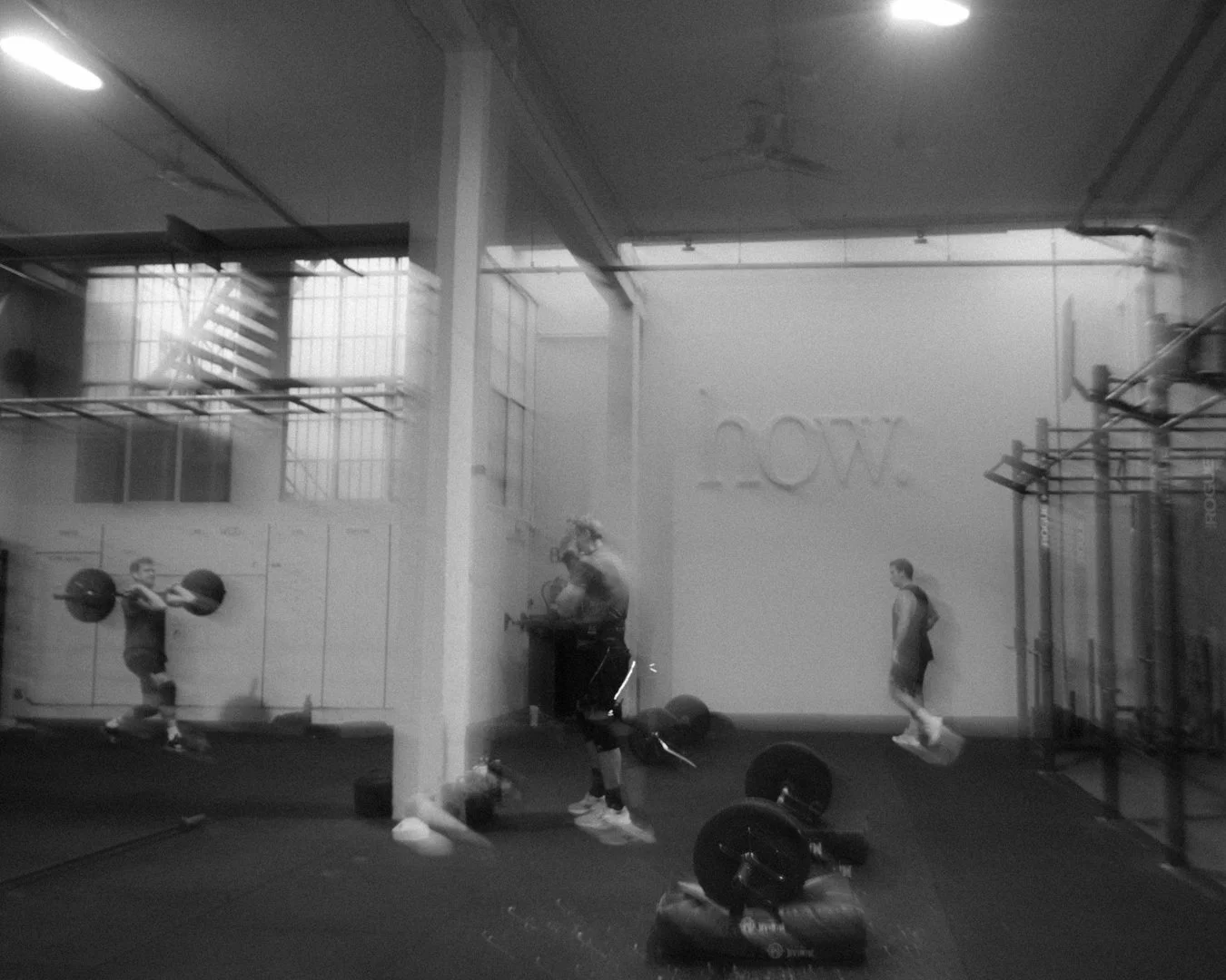 Una sala de entrenamiento con varias personas levantando pesas y haciendo ejercicio en un gimnasio moderno con paredes de vidrio y tecnología de entrenamiento.