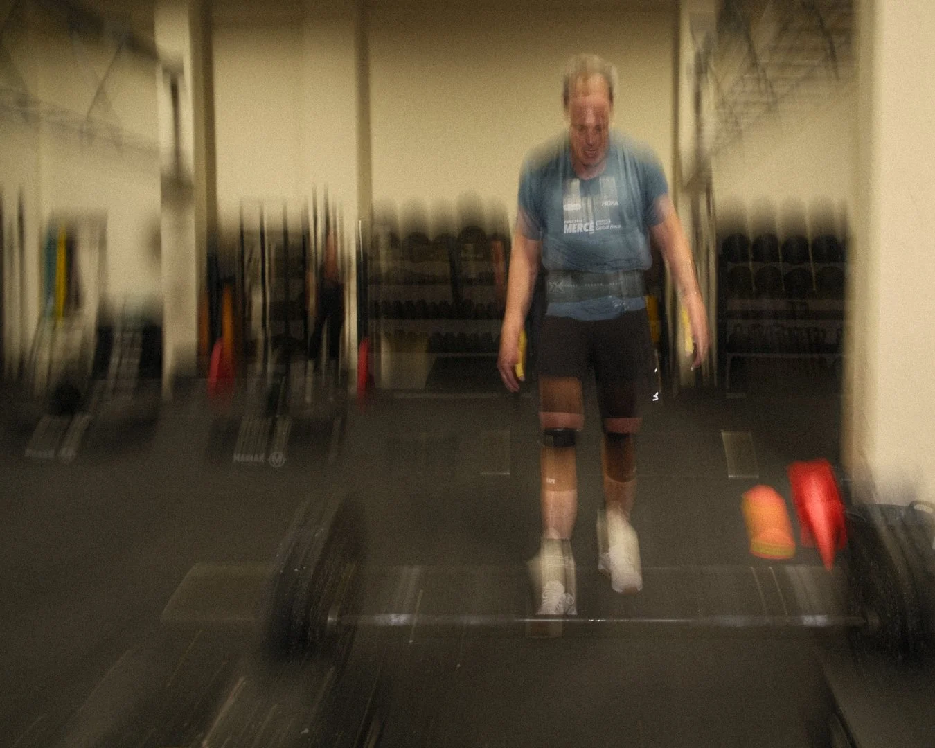 Persona en el gimnasio levantando pesas con movimiento borroso y fondo de máquinas de ejercicio.