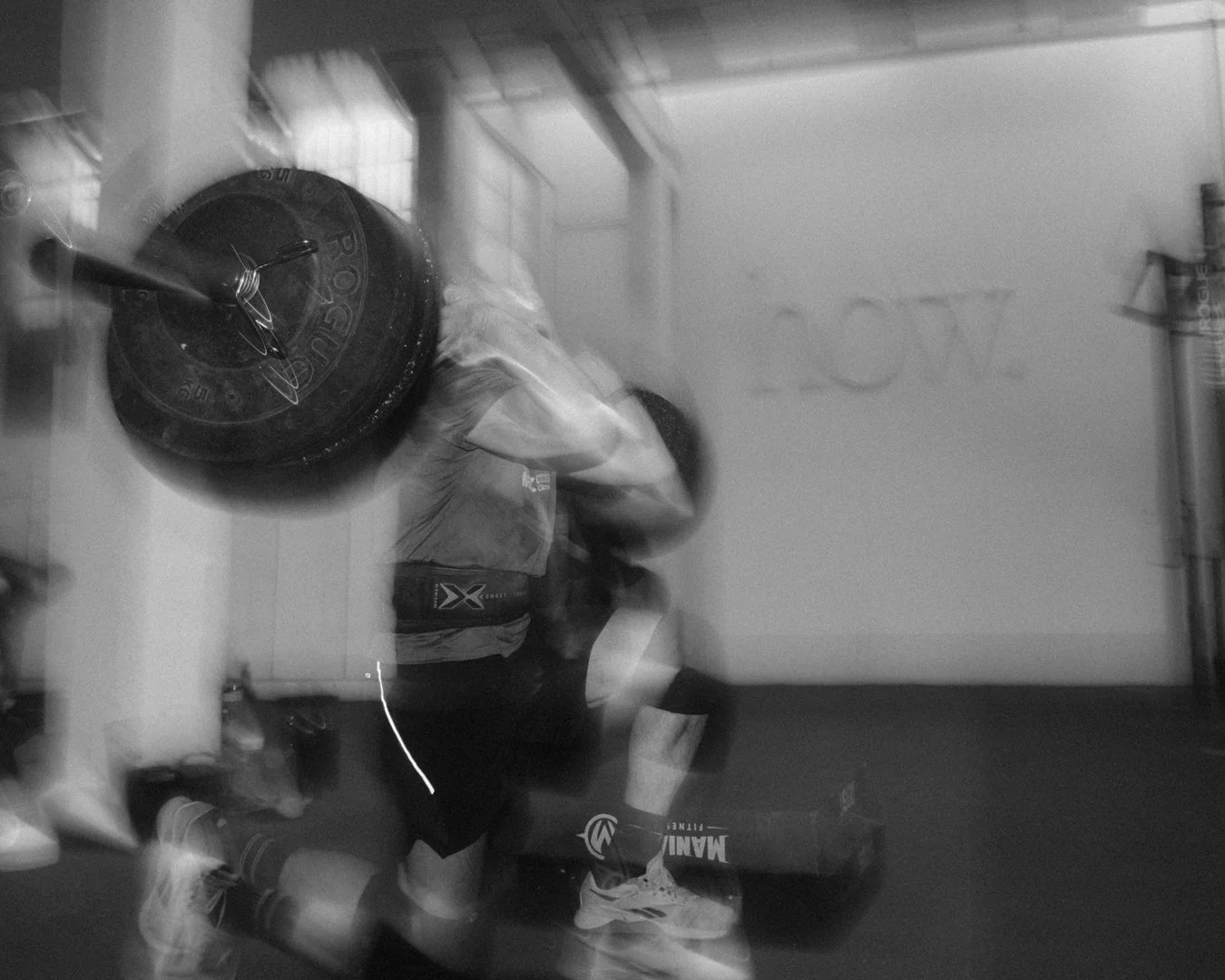 Personas levantando pesas en un gimnasio, reflejada en un espejo, en un entorno de entrenamiento con peso.