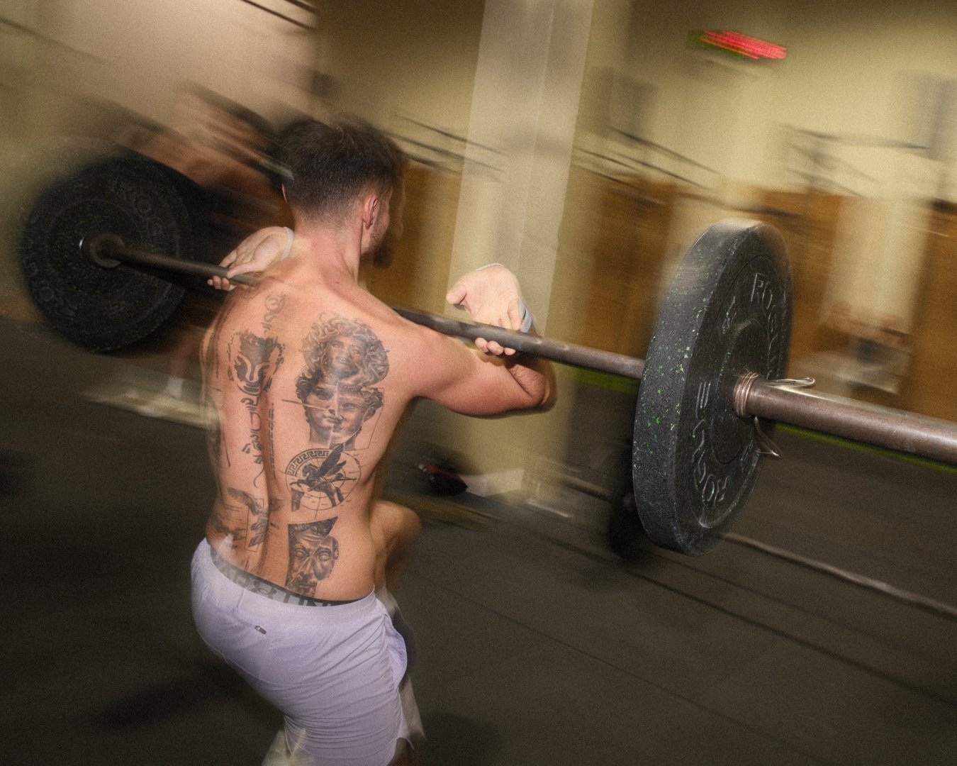 Hombre sin camisa con tatuajes levantando una barra con pesas en el gimnasio.