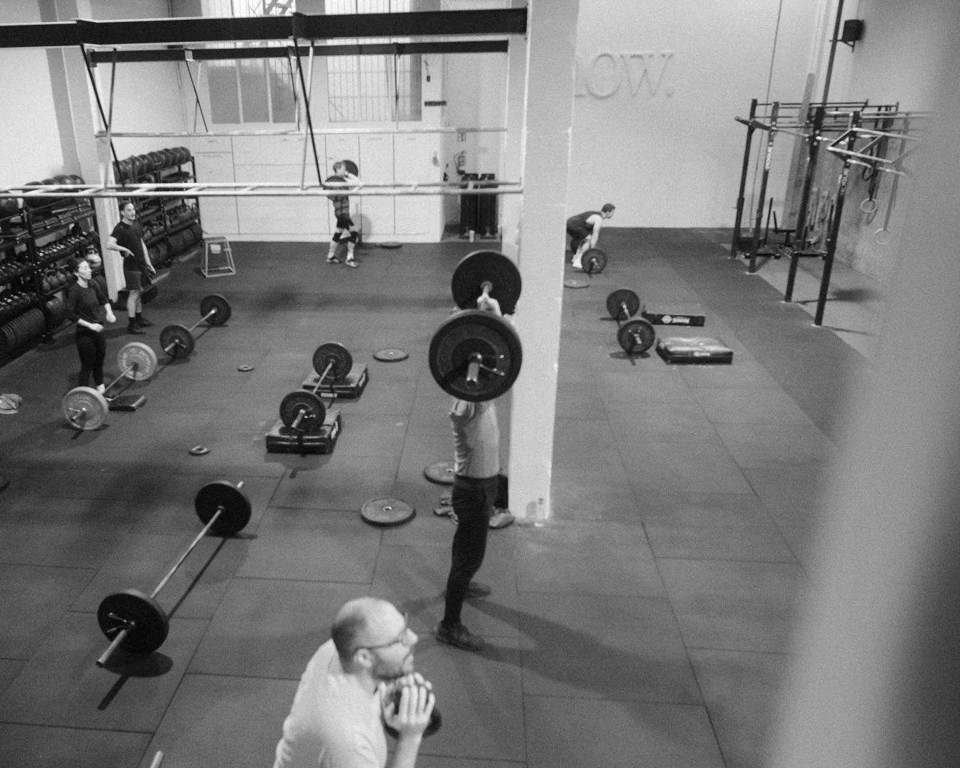 Gente haciendo levantamiento de pesas en un gimnasio con pesas y equipos en el fondo.