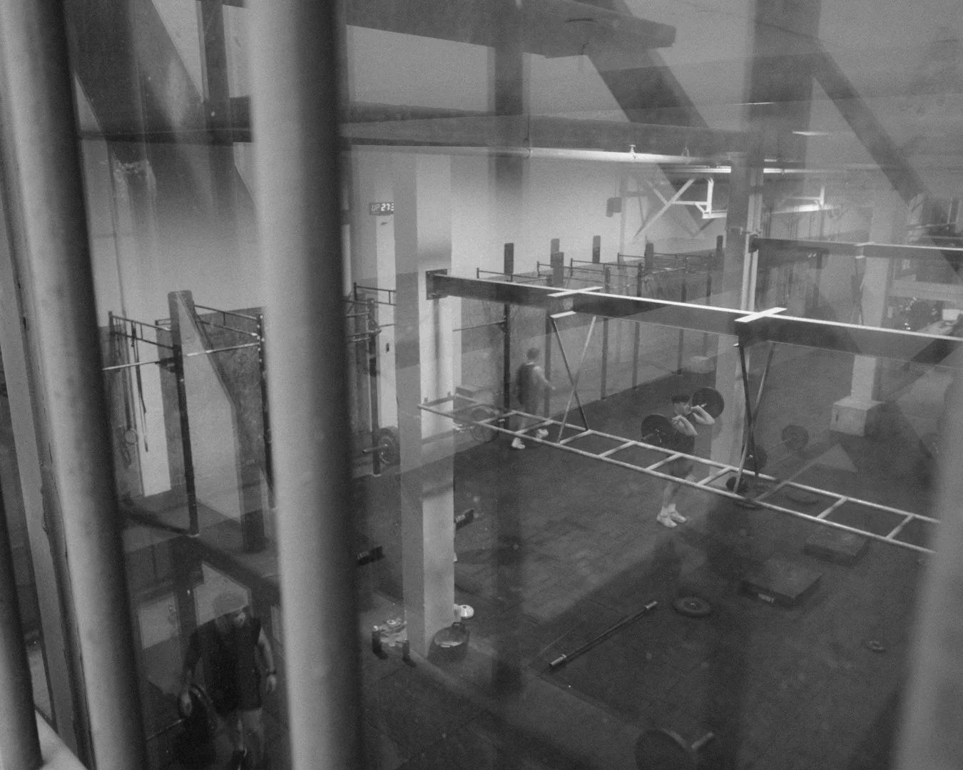 Personas entrenando en un gimnasio con equipo de ejercicio, visto desde una ventana de vidrio.