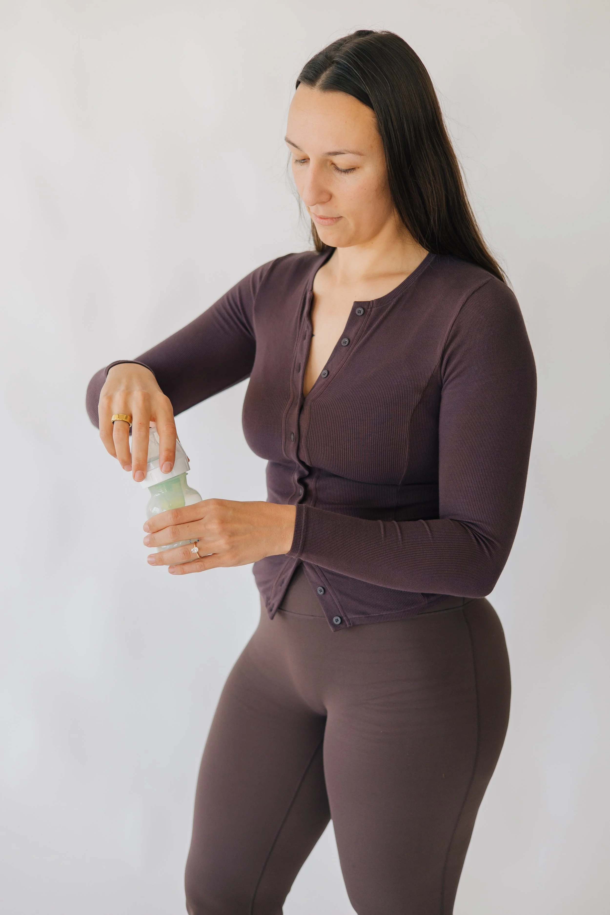 Woman in a dark purple long-sleeve shirt and brown pants opening a bottle of baby powder.