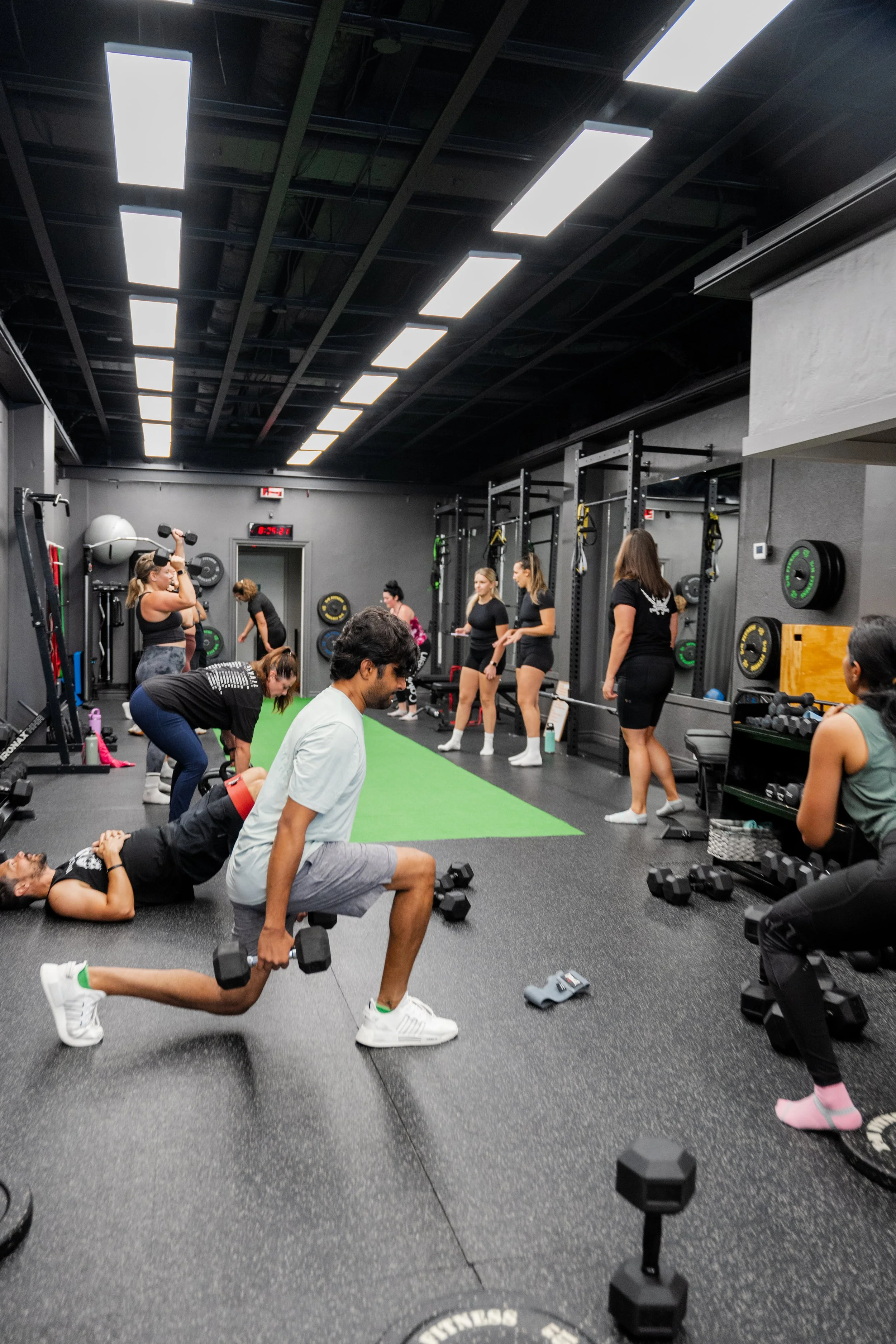 People working out in a gym with various exercise equipment and weights, some lifting weights and others using resistance bands.