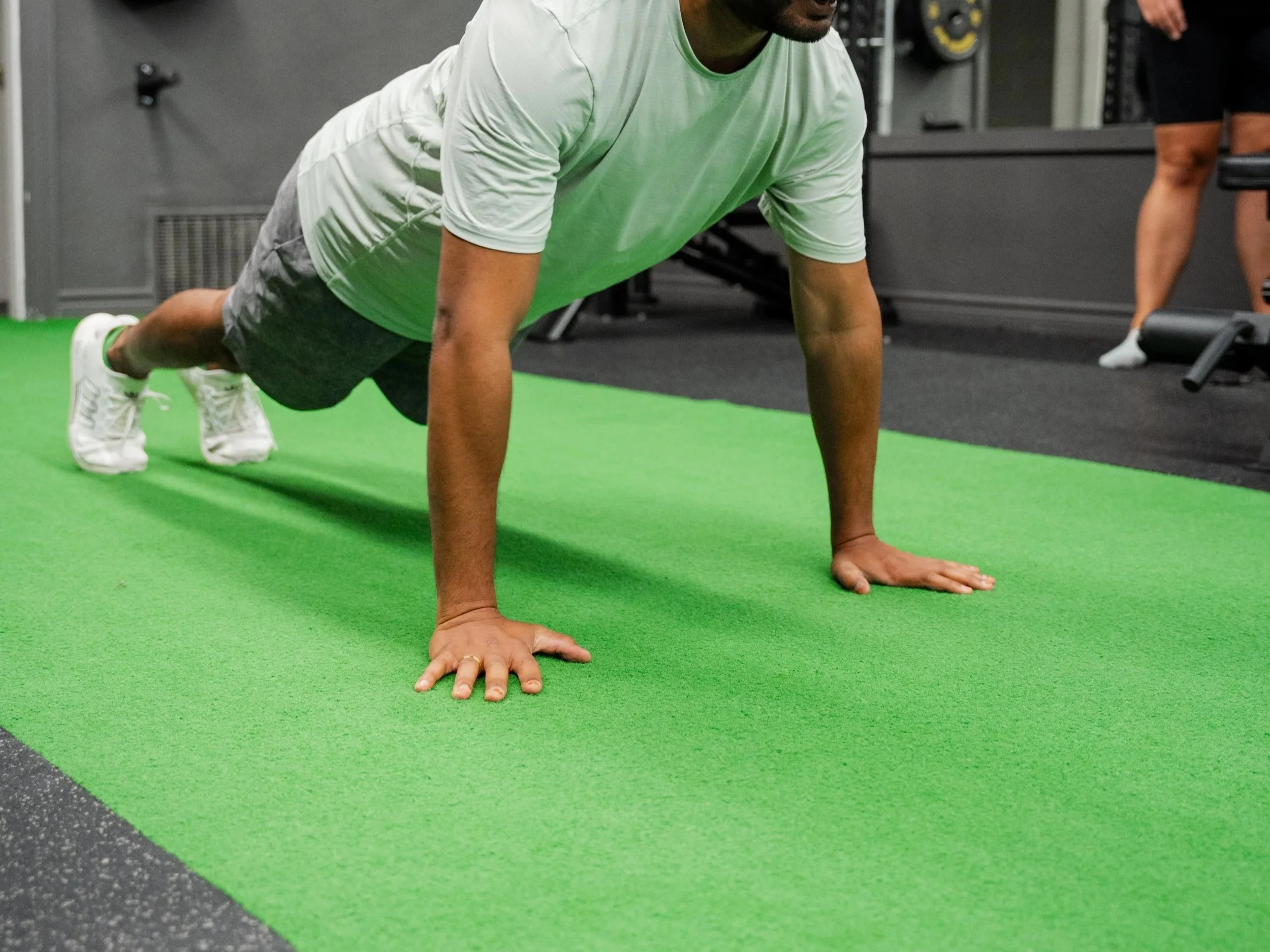 Man doing push-ups on a green exercise mat in a gym.