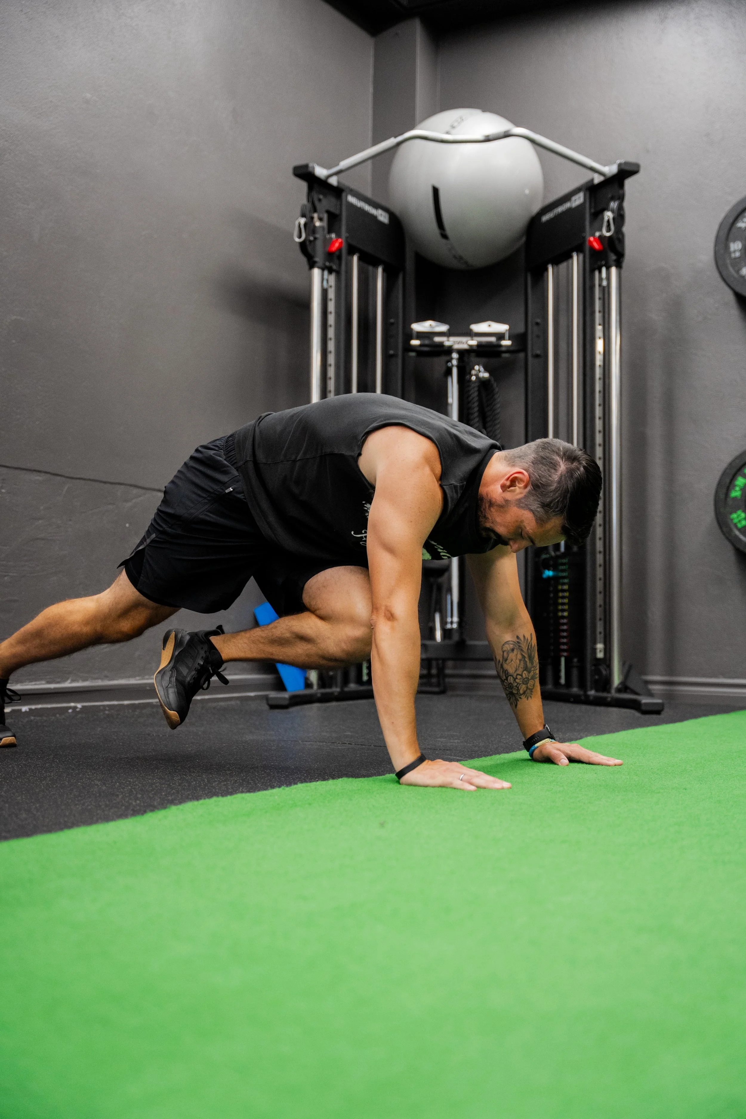 A man performing a mountain climber exercise in a gym, on a green mat with gym equipment in the background.