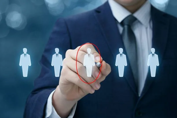 Businessman in suit drawing a red circle around a figure representing a person on a digital touch screen, with other figures faintly visible in the background.