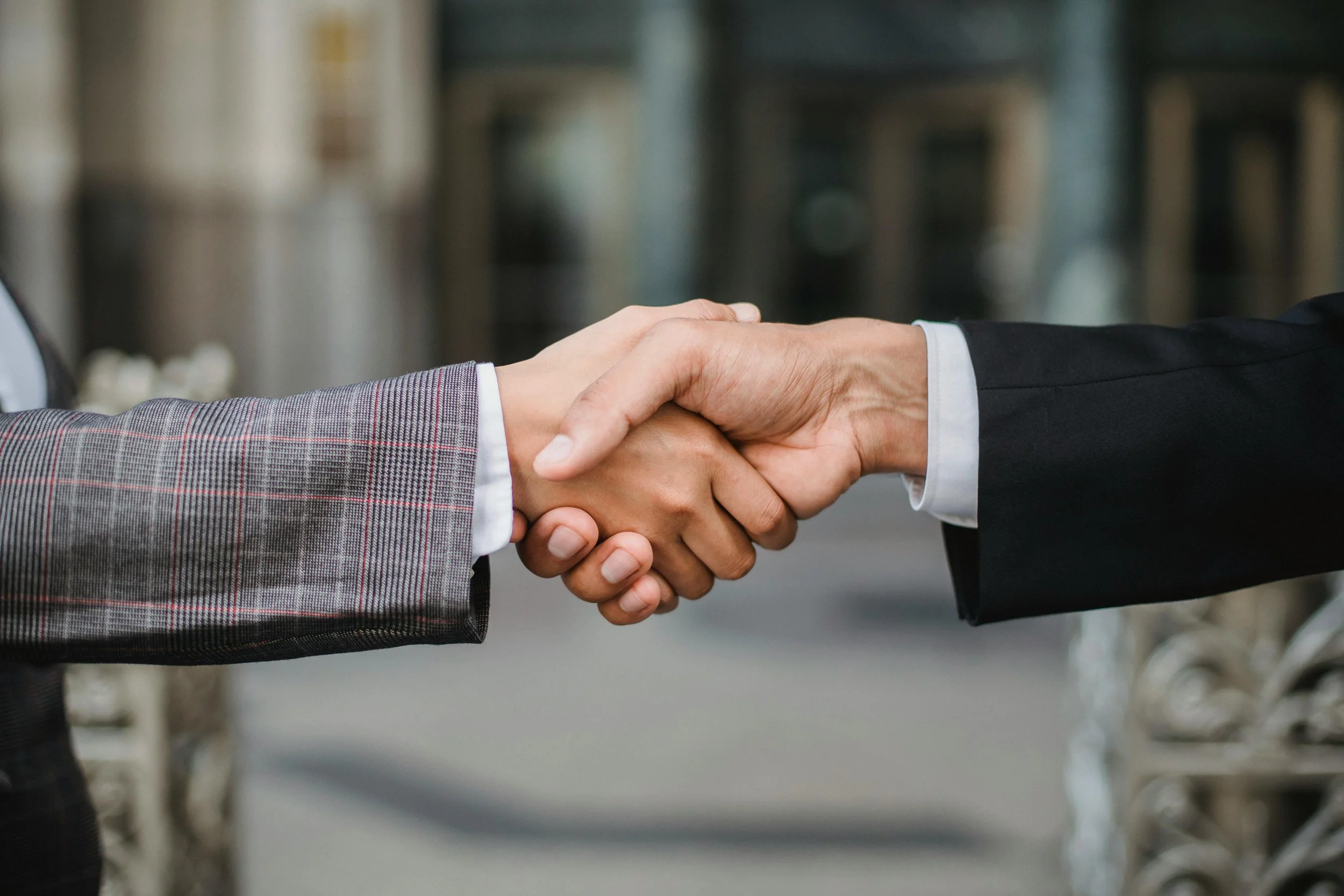 Close-up of two people in business attire shaking hands outside.