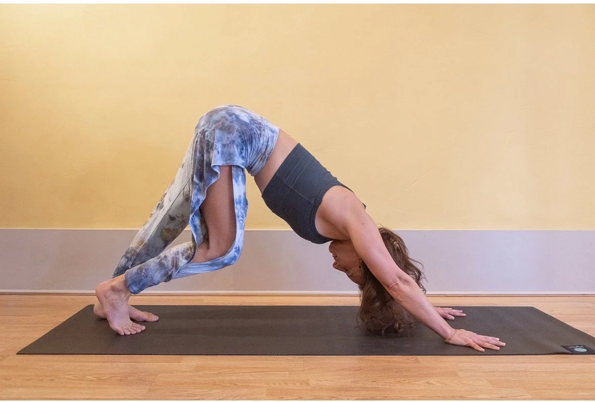 Woman practicing yoga in downward dog pose on a black yoga mat indoors.