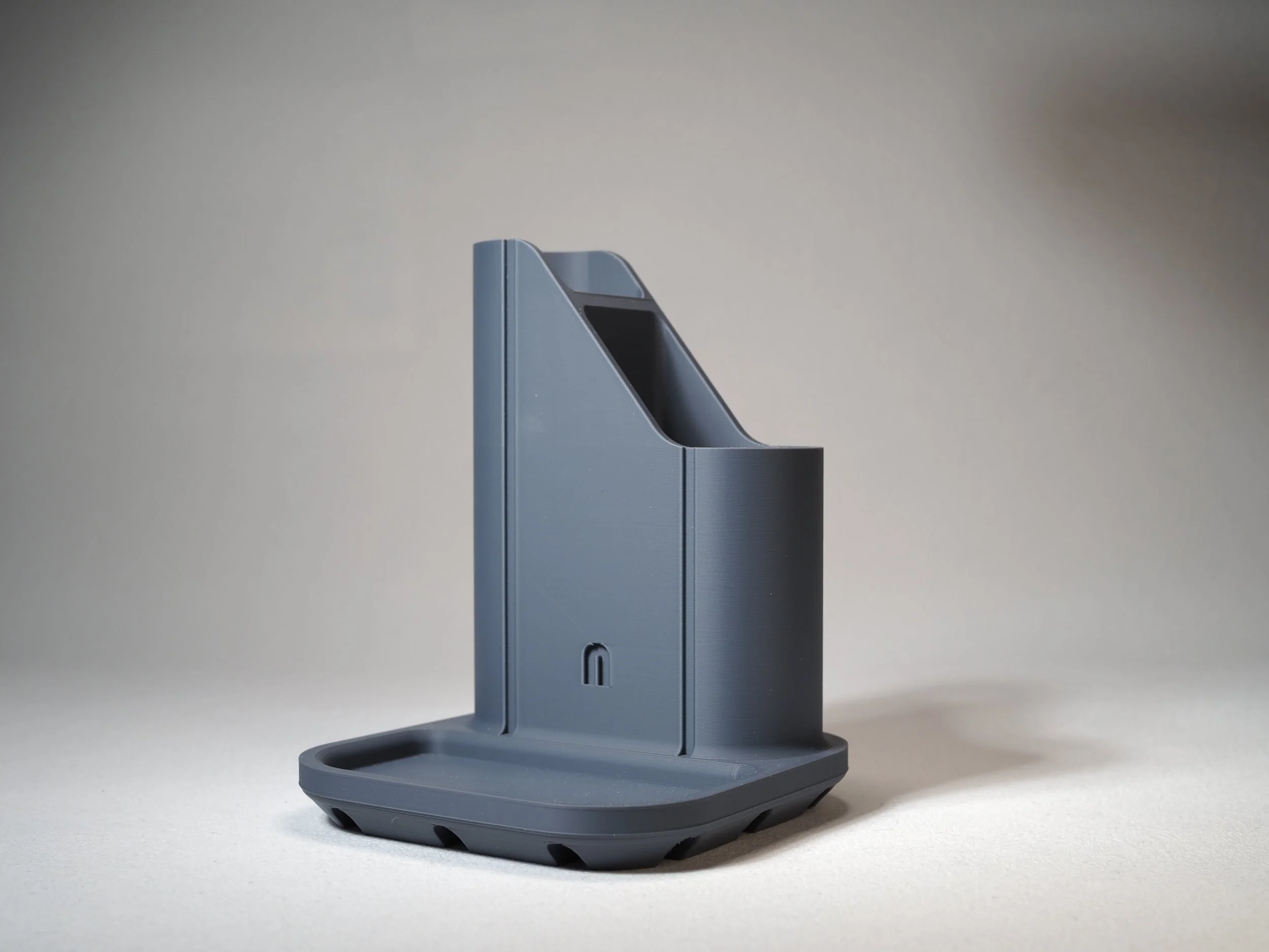 A gray 3D-printed holder with a slot on top, standing on a flat surface against a plain background.