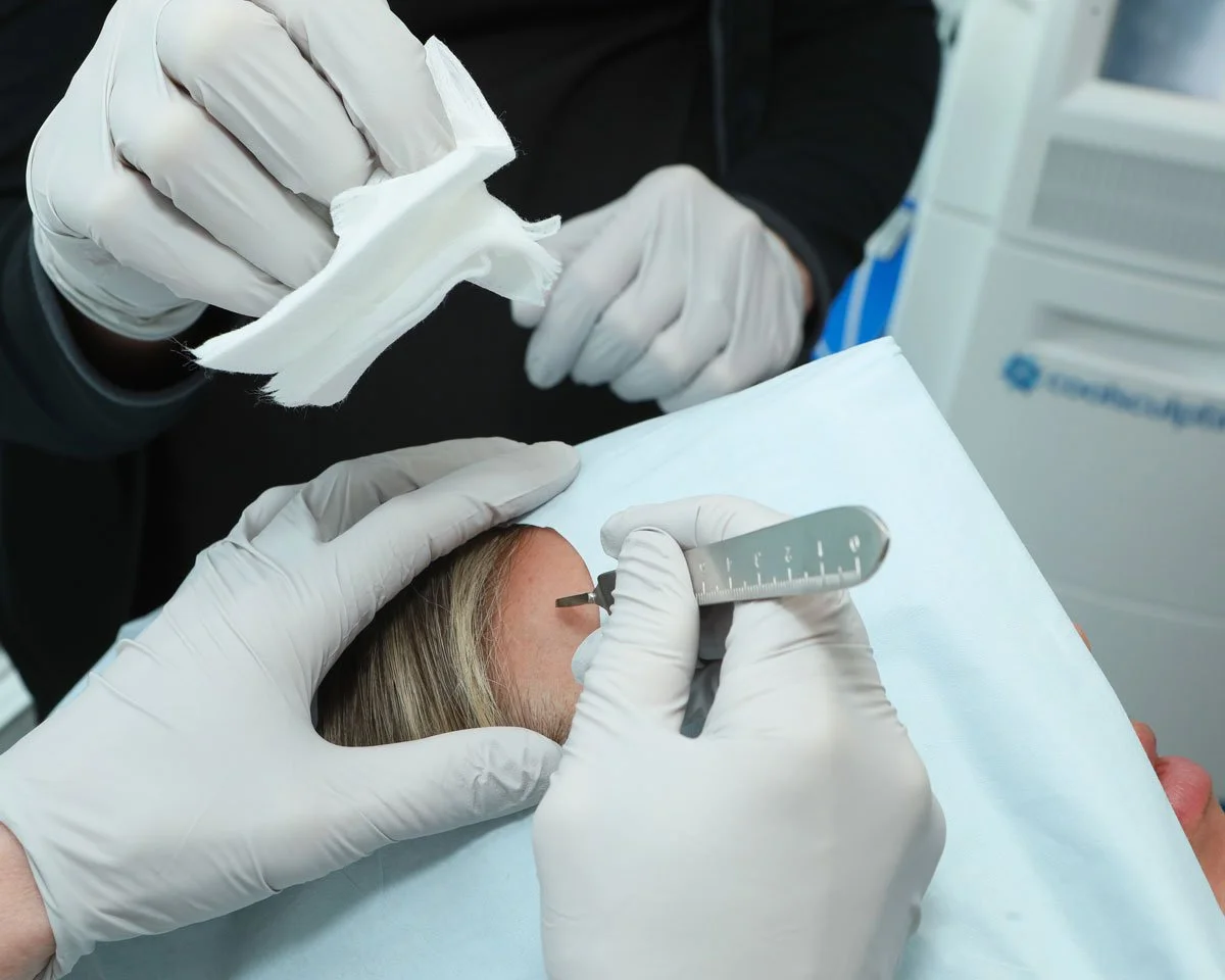 A person receiving a medical injection in their forehead with a syringe, while a healthcare worker holds a cotton swab.