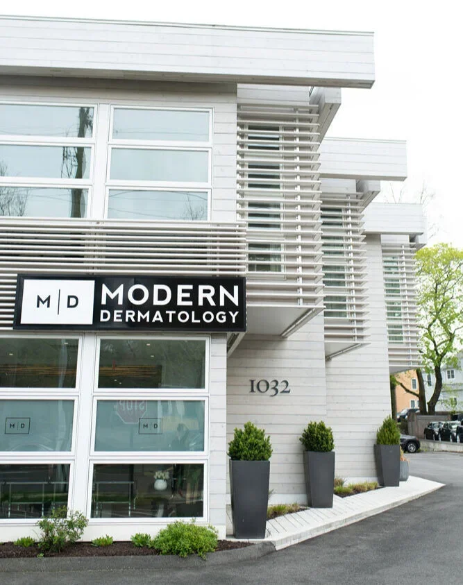 Modern building exterior with a sign for Modern Dermatology, three large planters with bushes, and the address 1032.