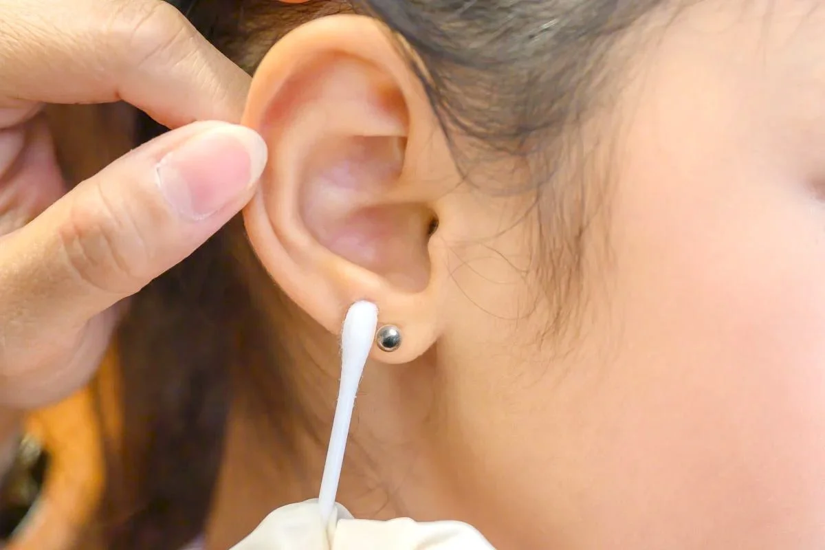 Close-up of a person with a pierced ear receiving ear hygiene cleaning with a cotton swab.