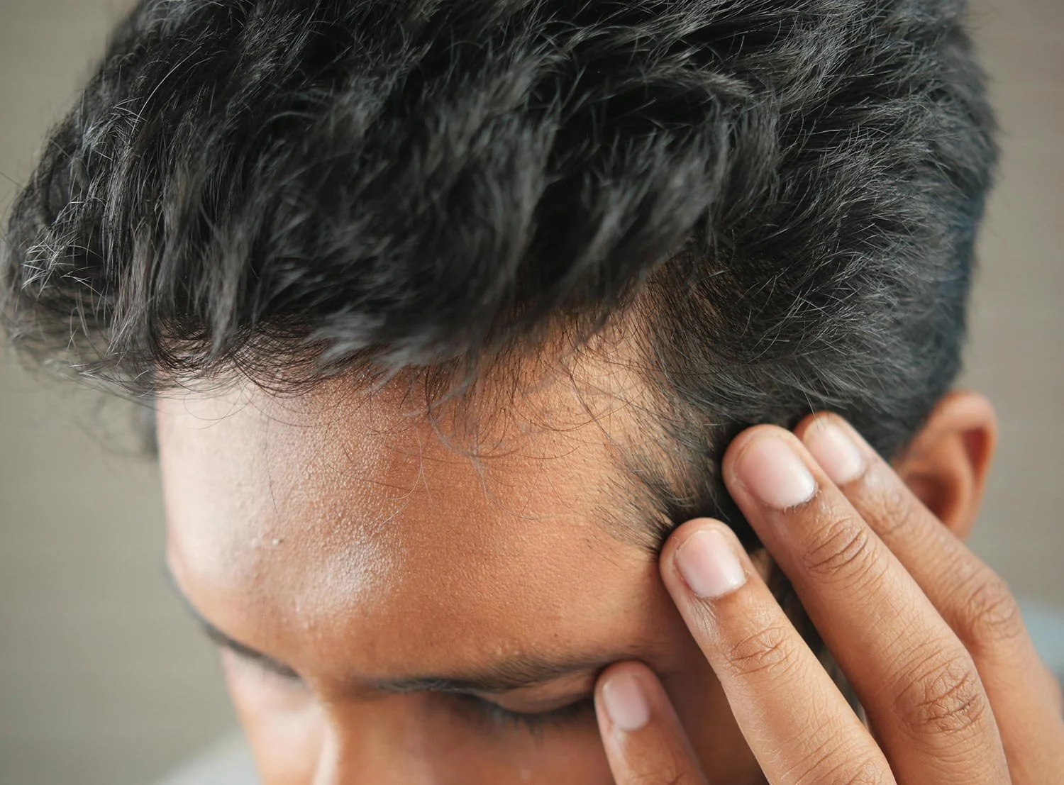 Close-up of a person touching their forehead with their hand, with dark, slightly wavy hair partially covering the head.