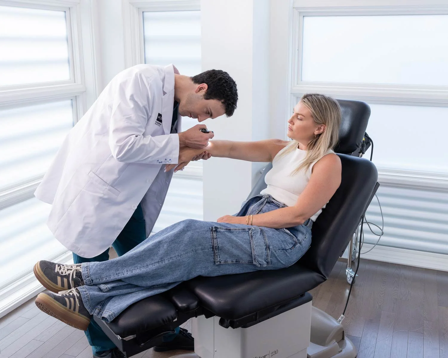 Doctor examining a woman's arm in a medical office, with the woman sitting on an examination chair.