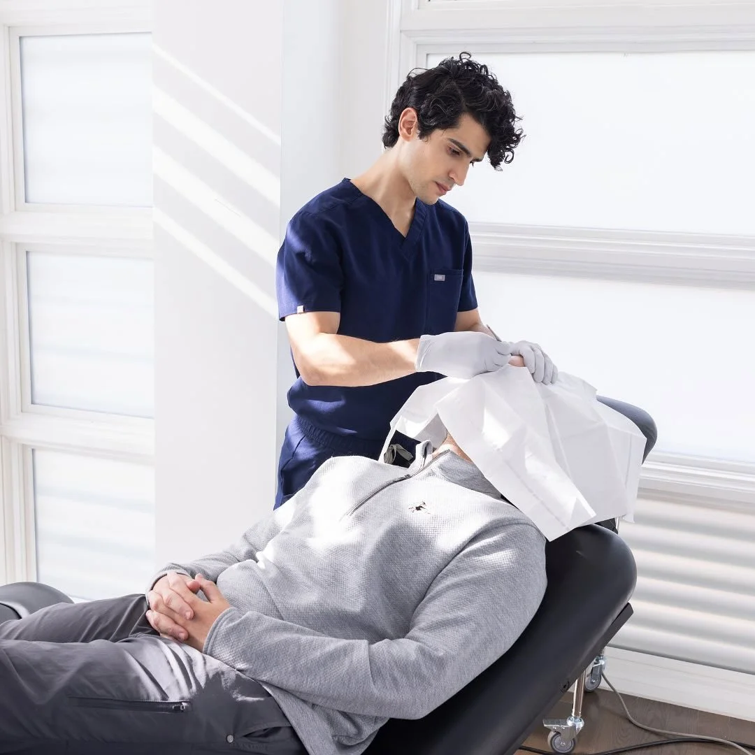 A healthcare professional performing a medical procedure on a patient lying on an examination table in a bright clinical setting.