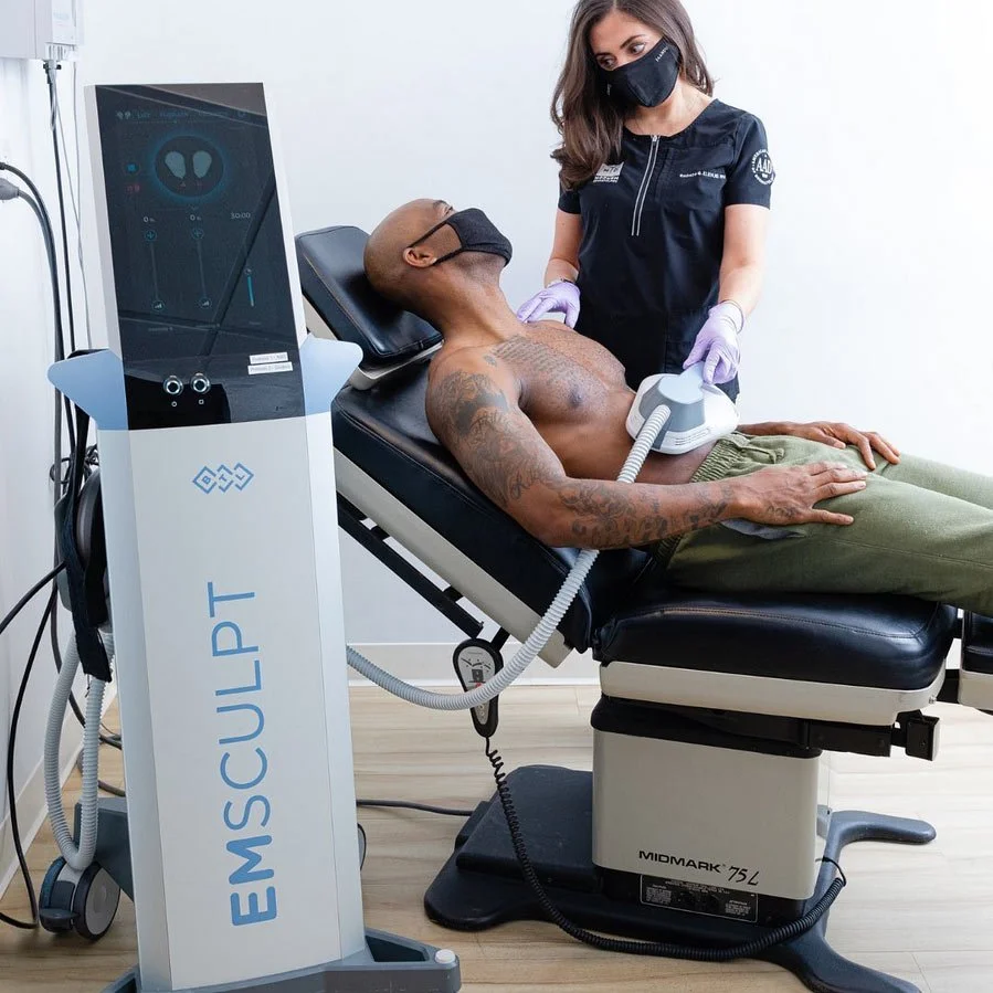 A man lying on an exam table receiving electromagnetic muscle stimulation from a healthcare professional in a clinical setting.