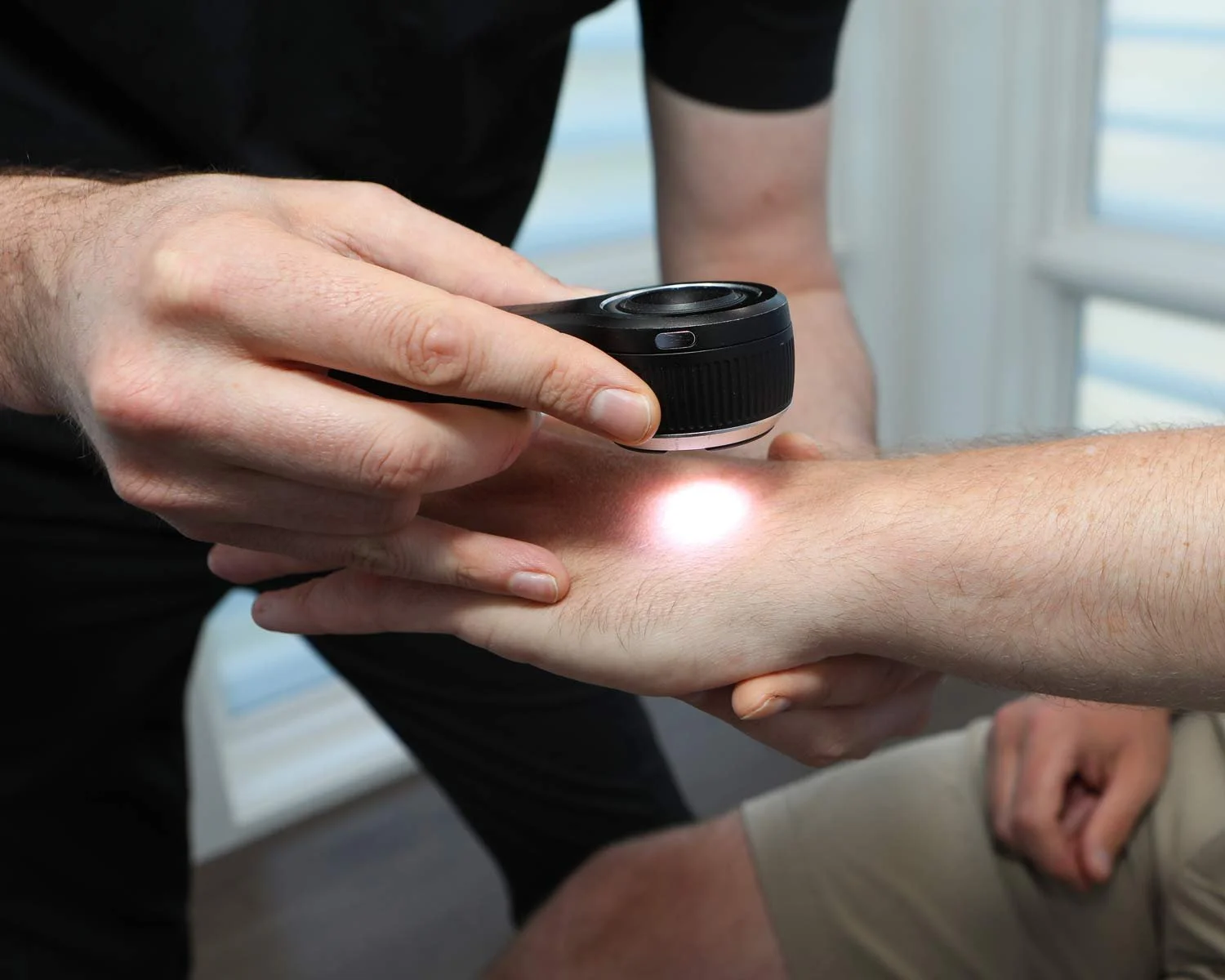 Healthcare professional examining a patient's skin using a handheld skin scanner with a light emission on the patient's arm.