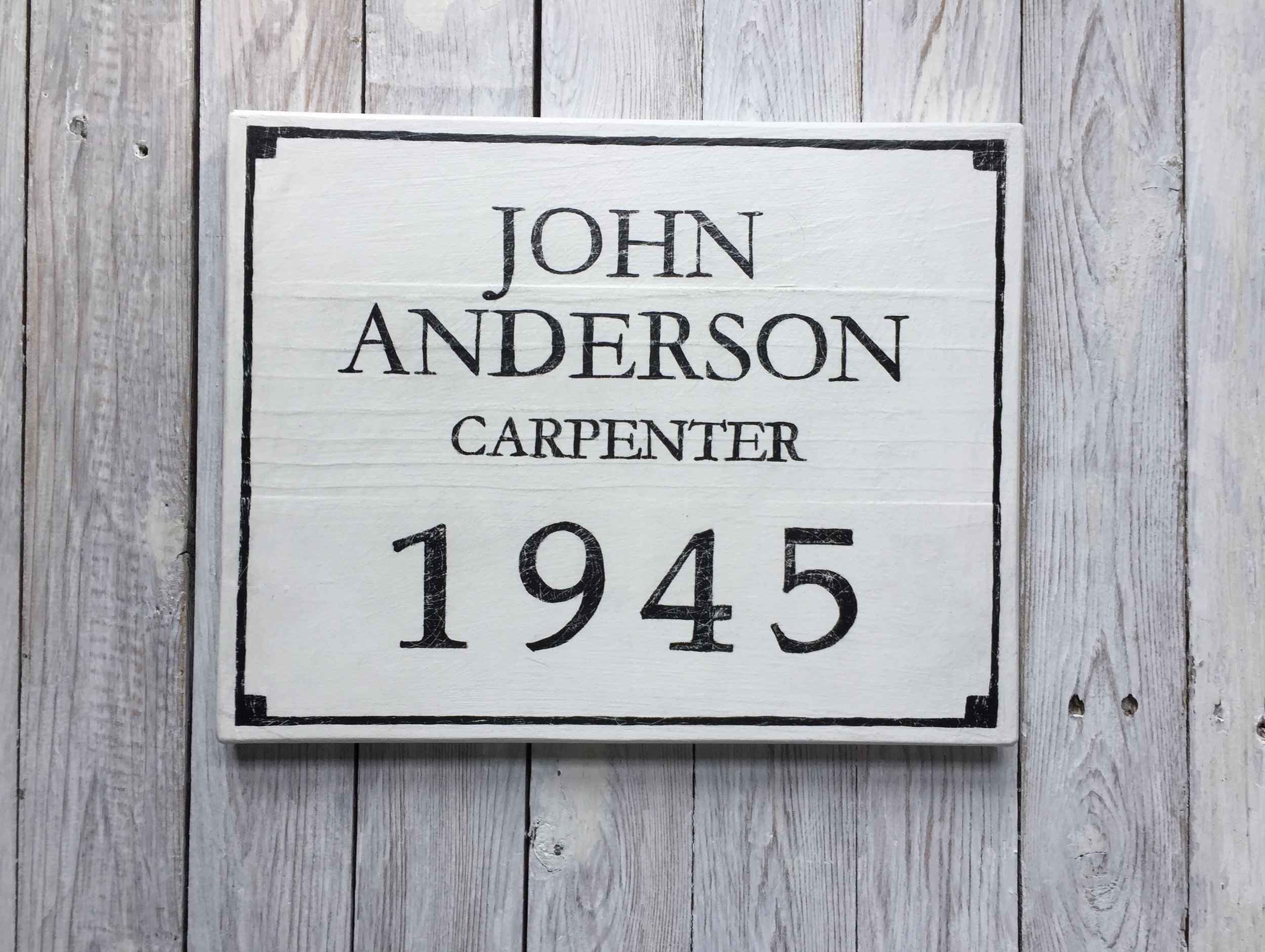 A white sign with black text that reads "JOHN ANDERSON CARPENTER 1945" 