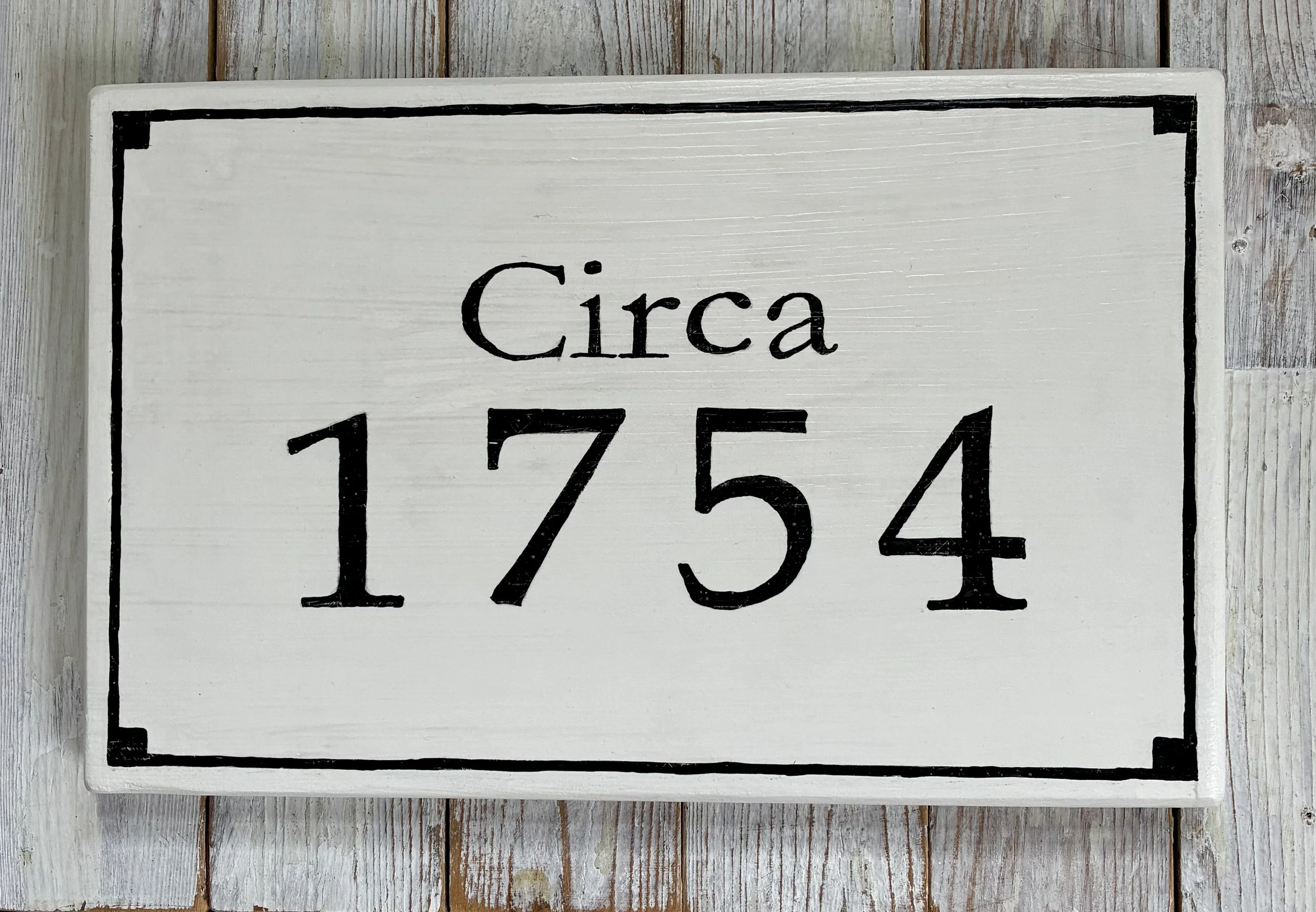 White wooden sign with black border and text that reads 'Circa 1754'.