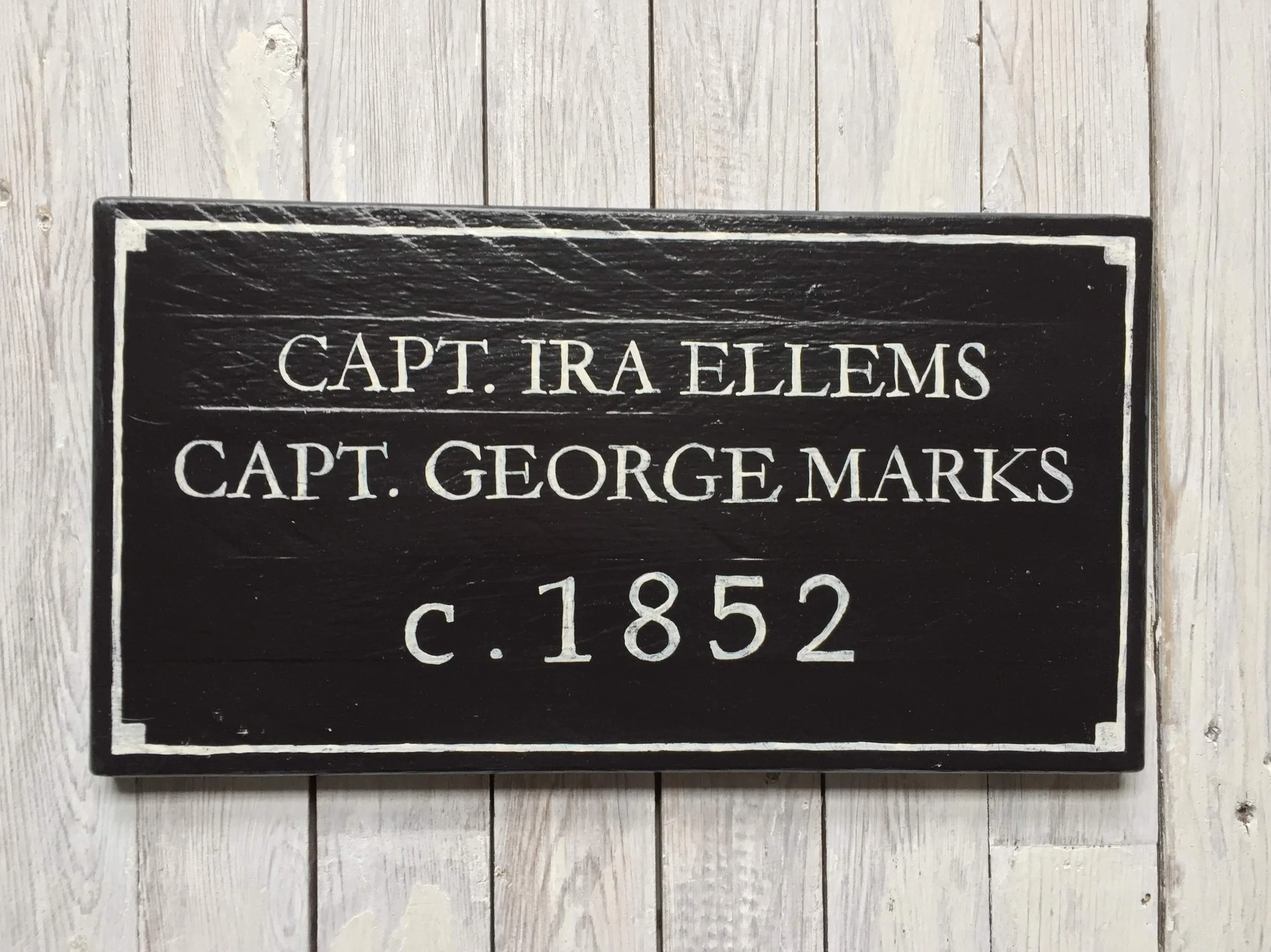 A black plaque with white text reading 'Capt. Ira Ellems, Capt. George Marks, c. 1852'