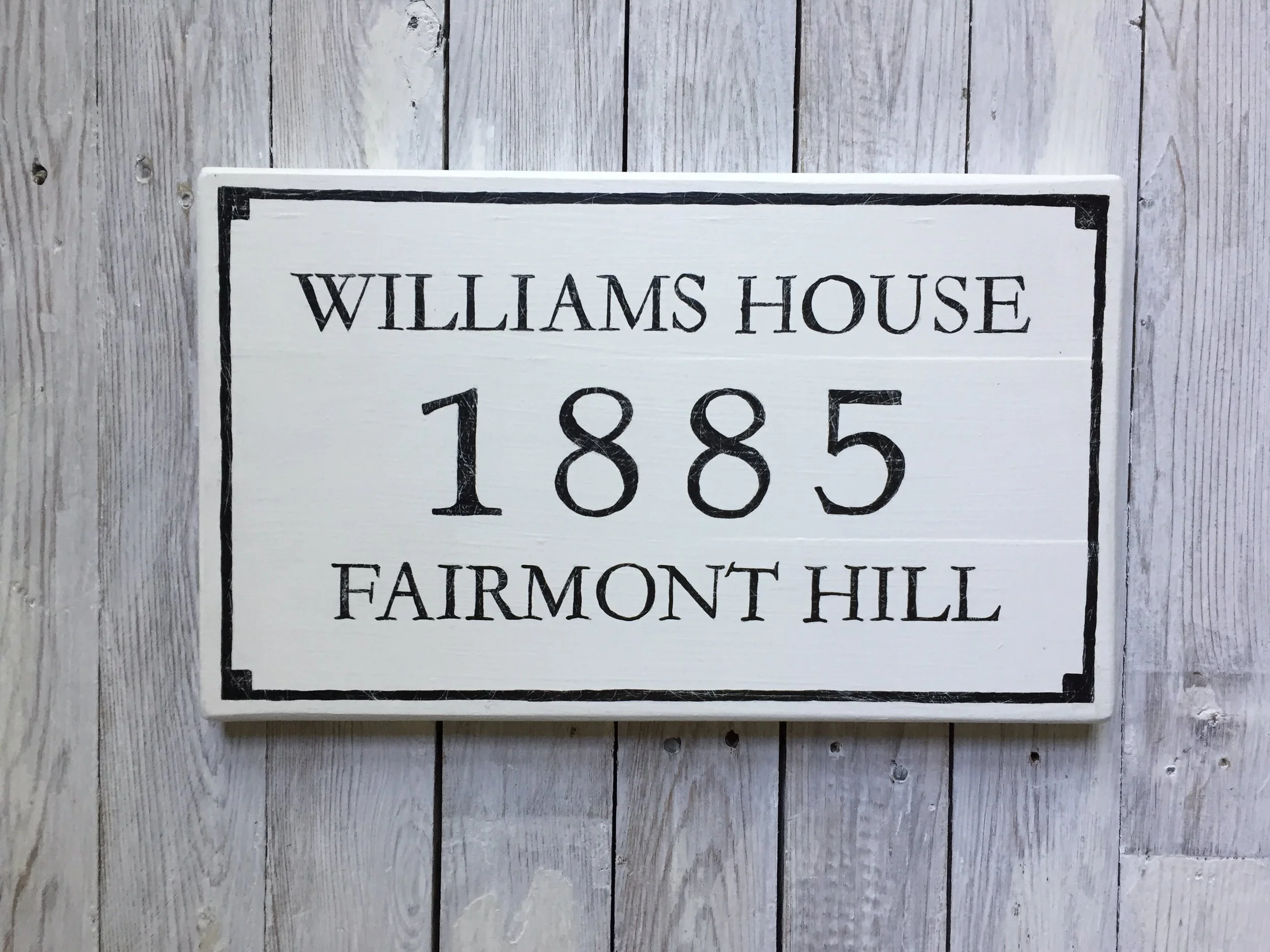 Wooden plaque with black border and text reading 'Williams House 1885 Fairmont Hill' 