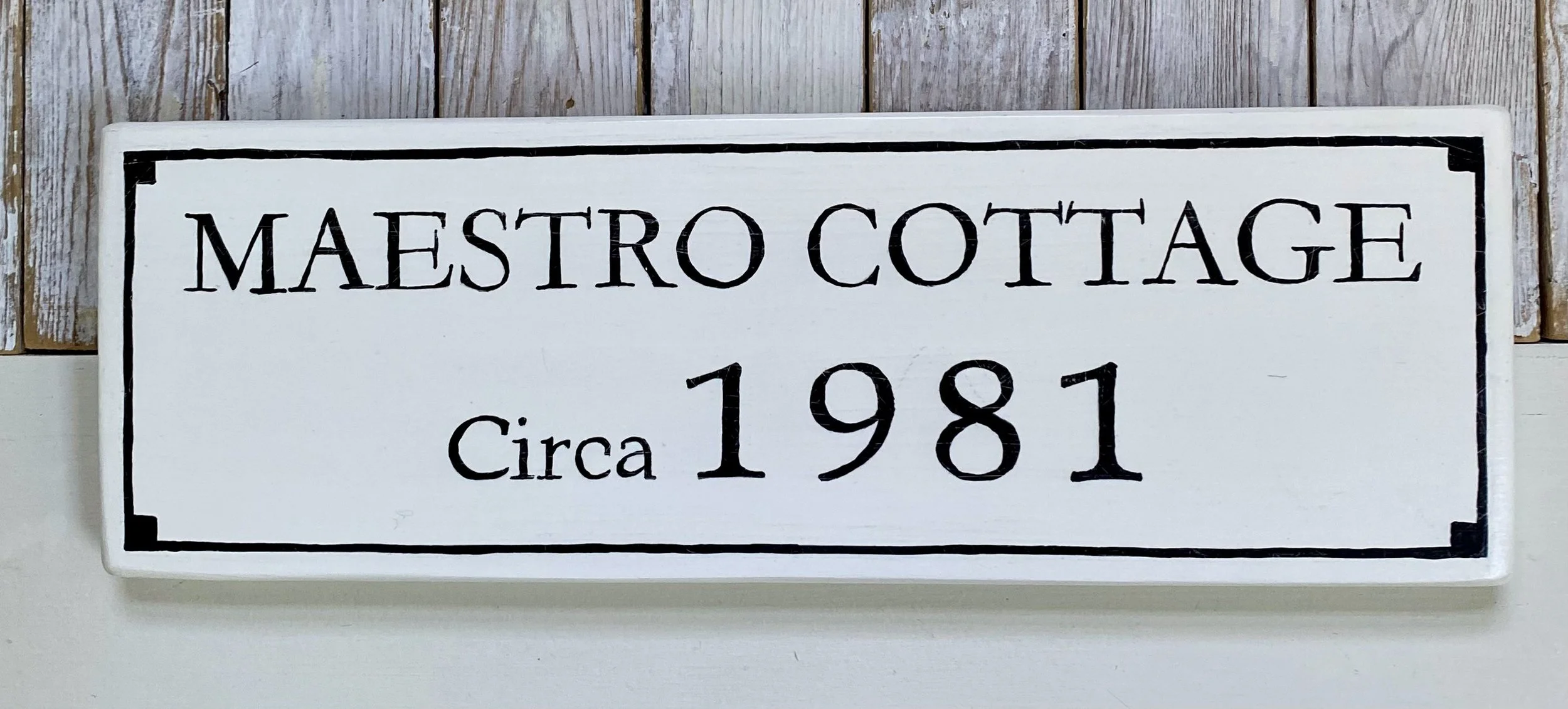 A white decorative sign with black border text reading 'Maestro Cottage Circa 1981' 