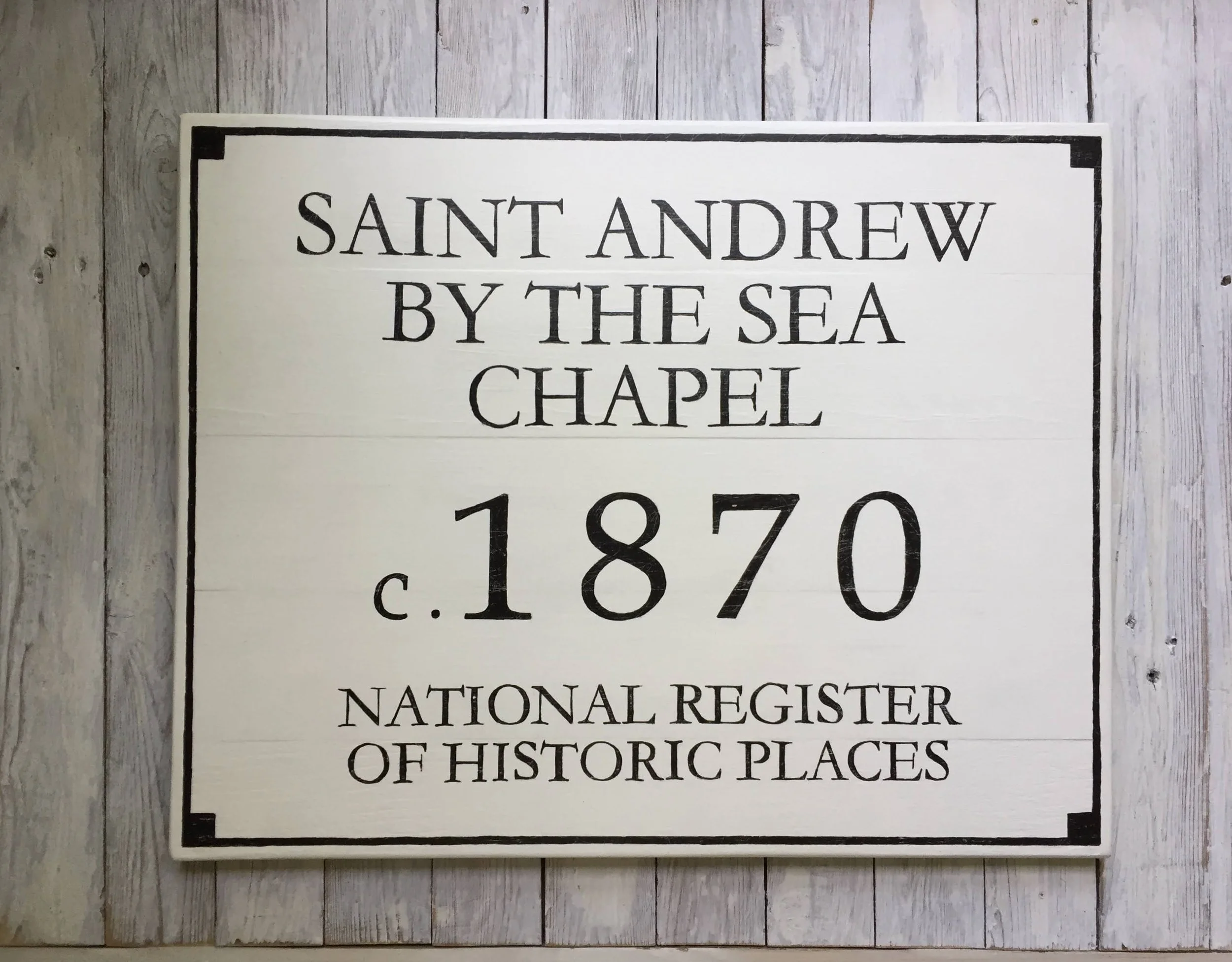 Sign with black text on white background stating 'Saint Andrew by the Sea Chapel, c. 1870, National Register of Historic Places' 