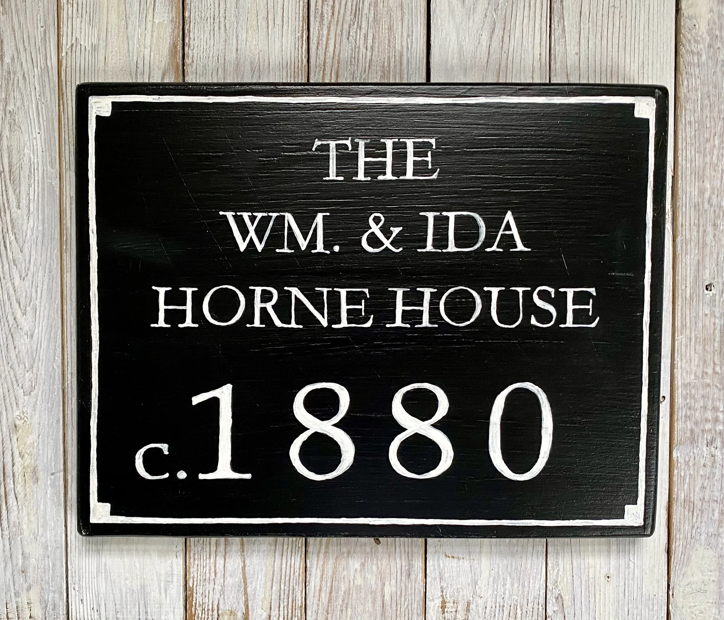 Black wooden sign with white lettering reading "The Wm. & Ida Horne House c.1880," mounted on a light wood wall.