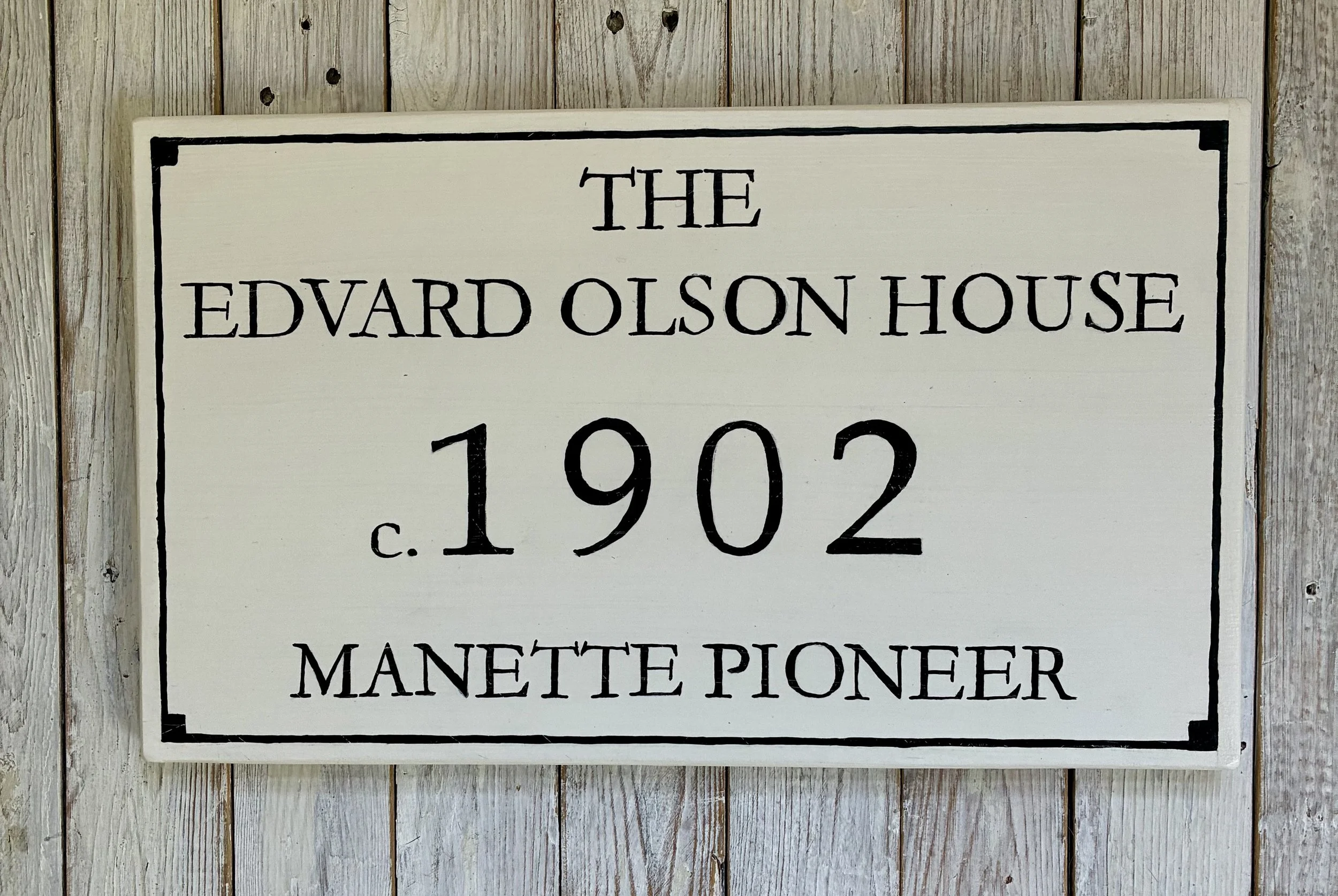 A rectangular sign with black text on a white background. The sign reads: "The Edvard Olson House c. 1902 Manette Pioneer."