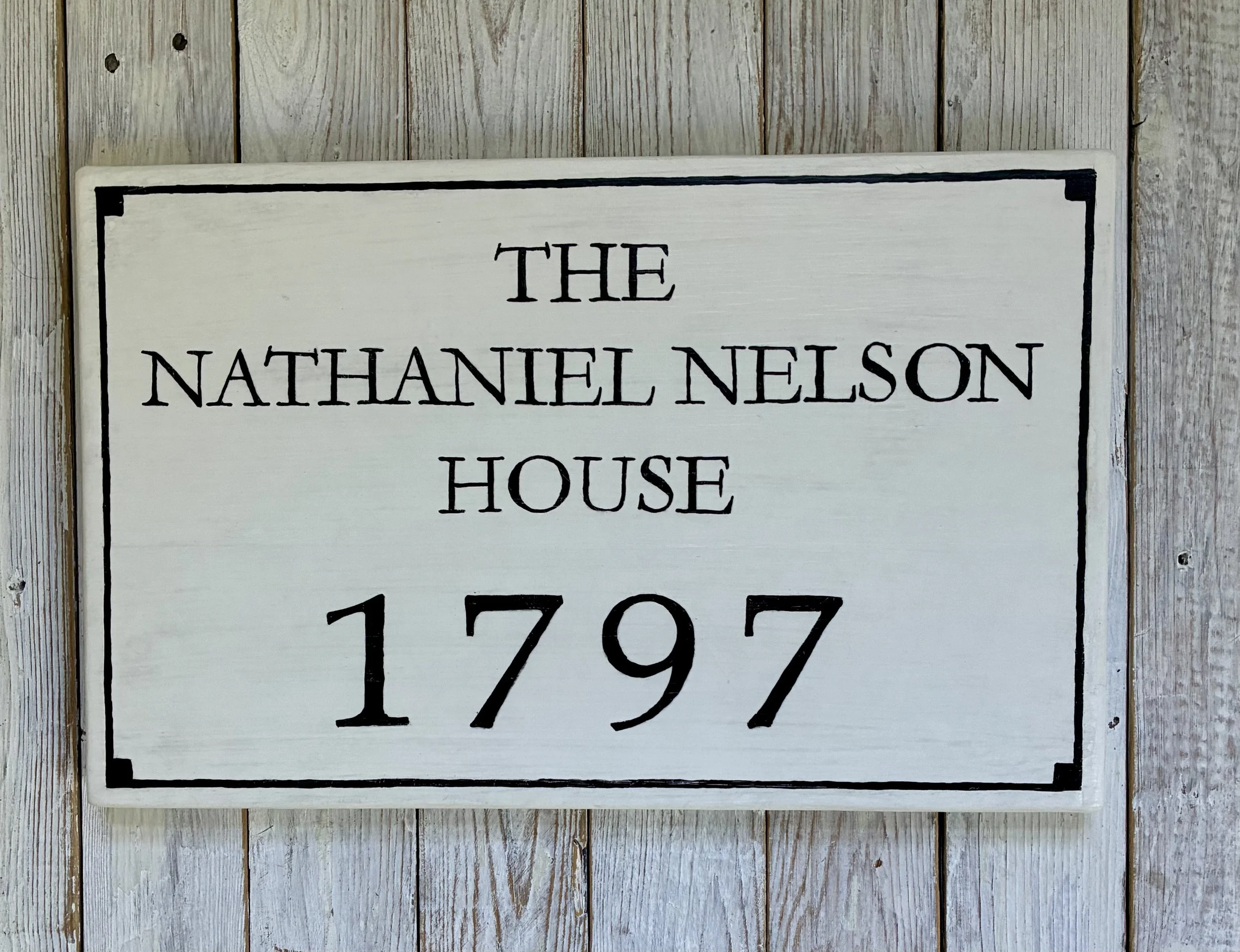 A white wooden sign that reads 'The Nathaniel Nelson House 1797' in black text