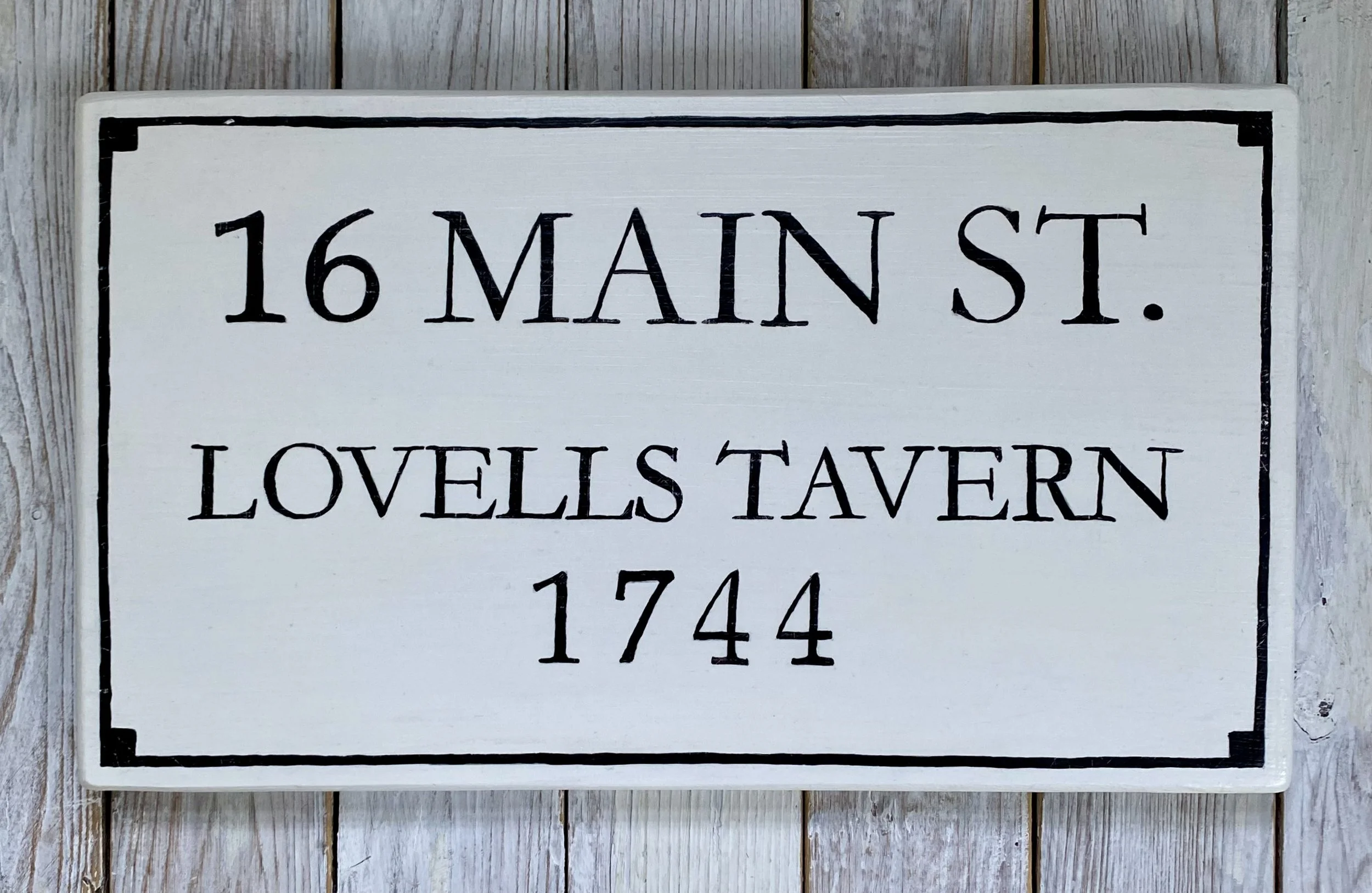 A white wooden sign with black address and text reading, '16 Main St., Lovells Tavern 1744'