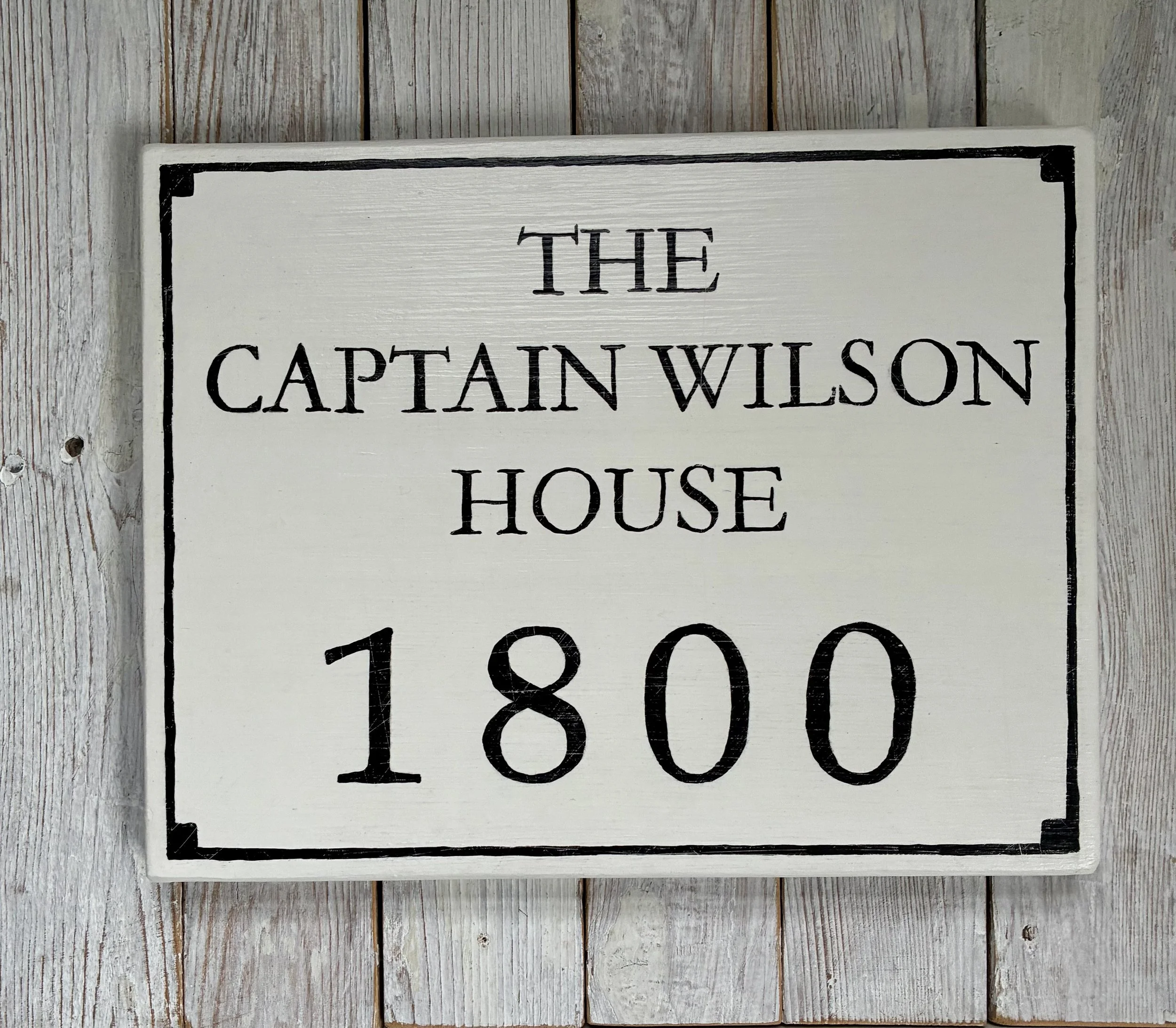 White wooden sign with black text reading 'The Captain Wilson House 1800,' 