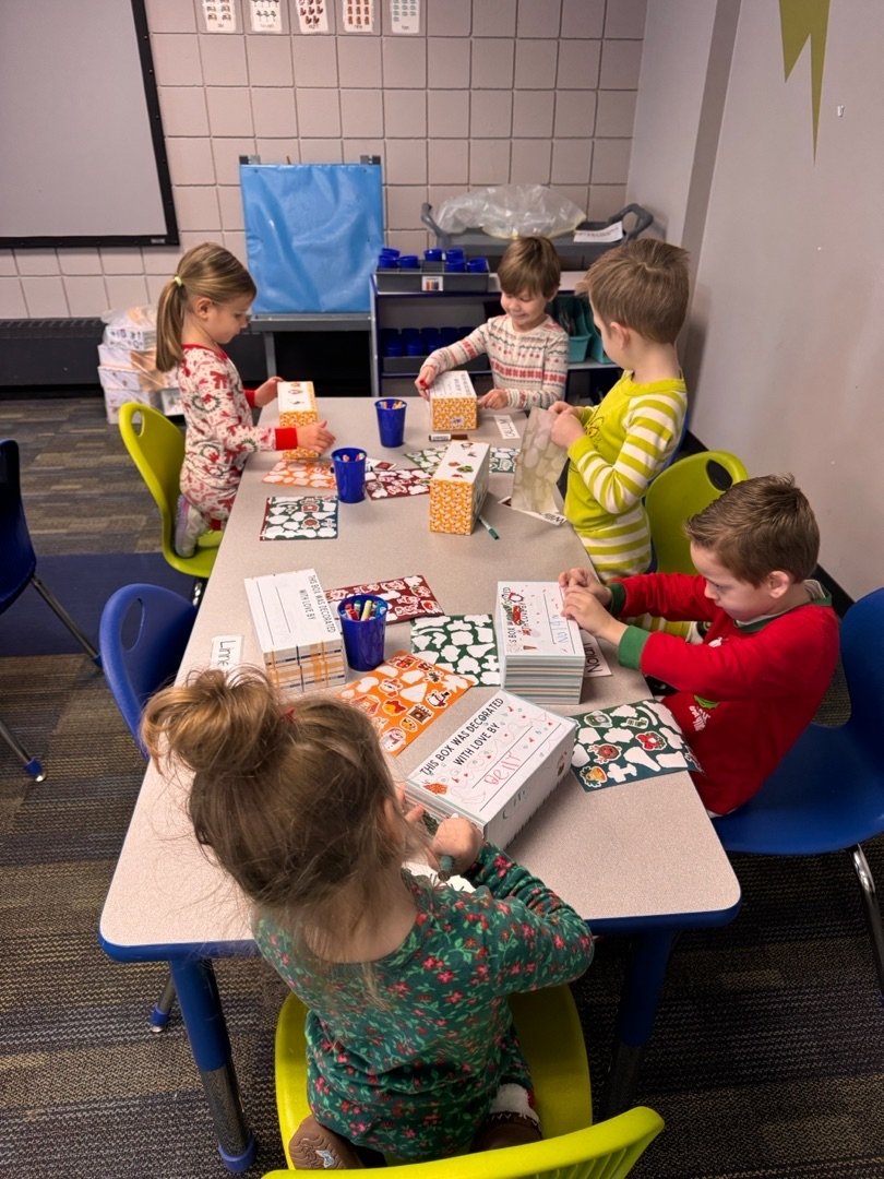 Children at a table wrapping presents with holiday-themed wrapping paper.