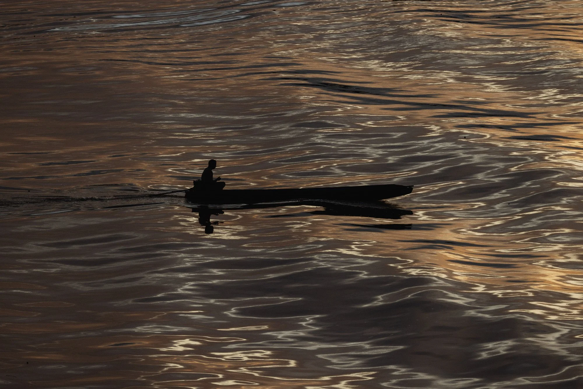 Silhouette eines Mannes in einem Kanu auf dem Amazonas bei Sonnenuntergang mit goldenen Lichtreflexionen auf dem Wasser, Breves, Brasilien.