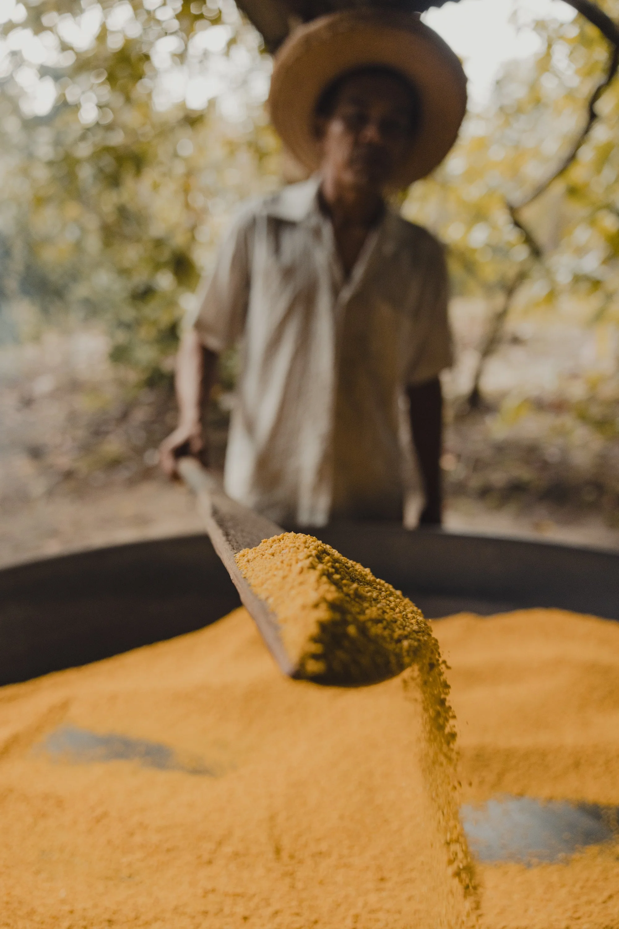 Person schaufelt gelbes Maniokmehl in einem großen Behälter.
