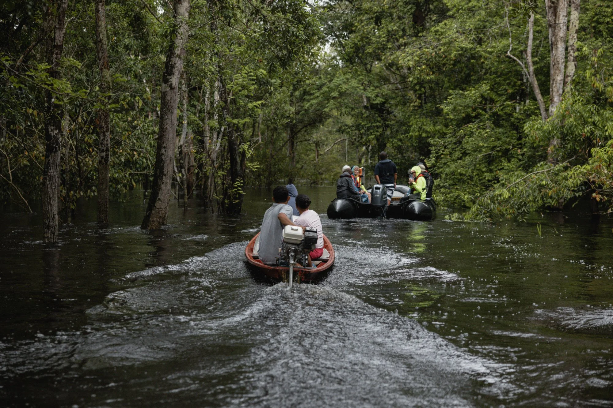Mehrere Boote fahren durch einen schmalen Regenwaldkanal.