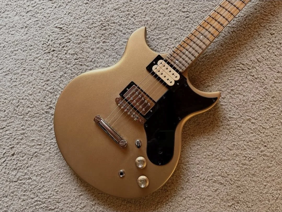 A gold-colored electric guitar with black pickguard and dual humbucker pickups, lying on a beige carpet.