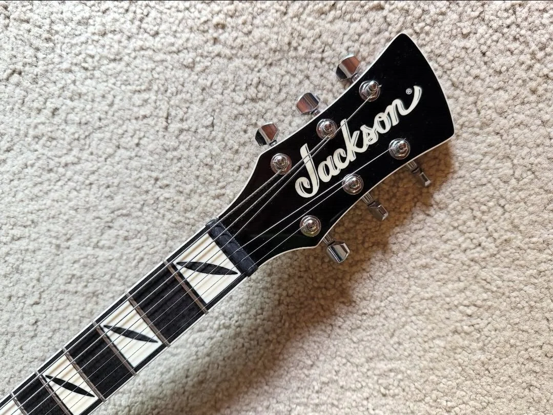 Close-up of a Jackson guitar headstock with tuning pegs, lying on a beige carpet.