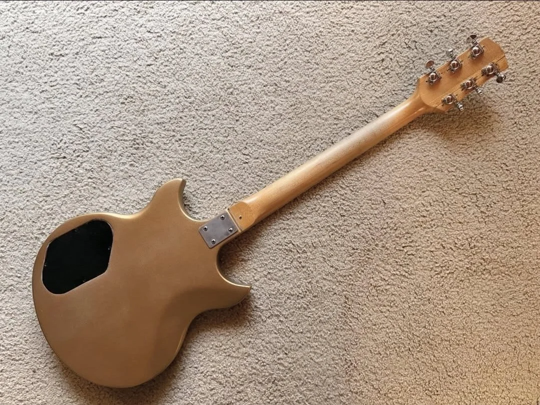 A light-colored electric guitar laying on a beige carpeted floor, showing the back of the instrument.