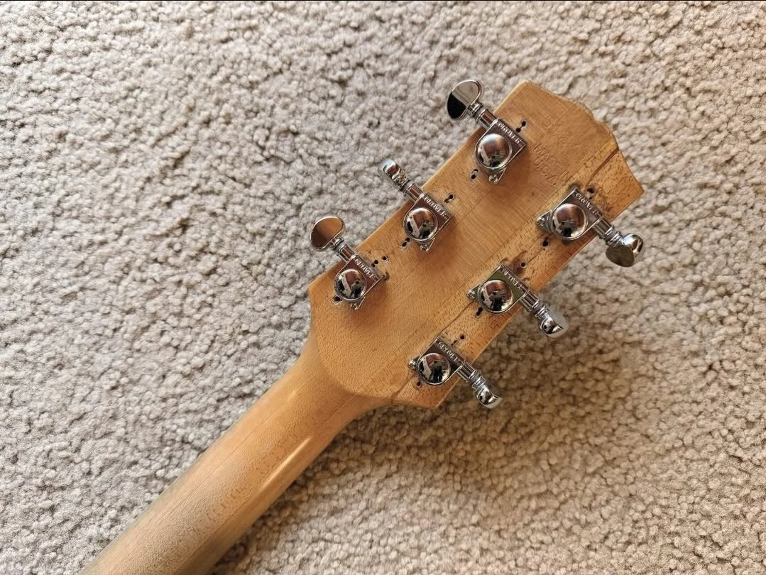Close-up of the back of a guitar headstock with tuning pegs, lying on a beige carpet.
