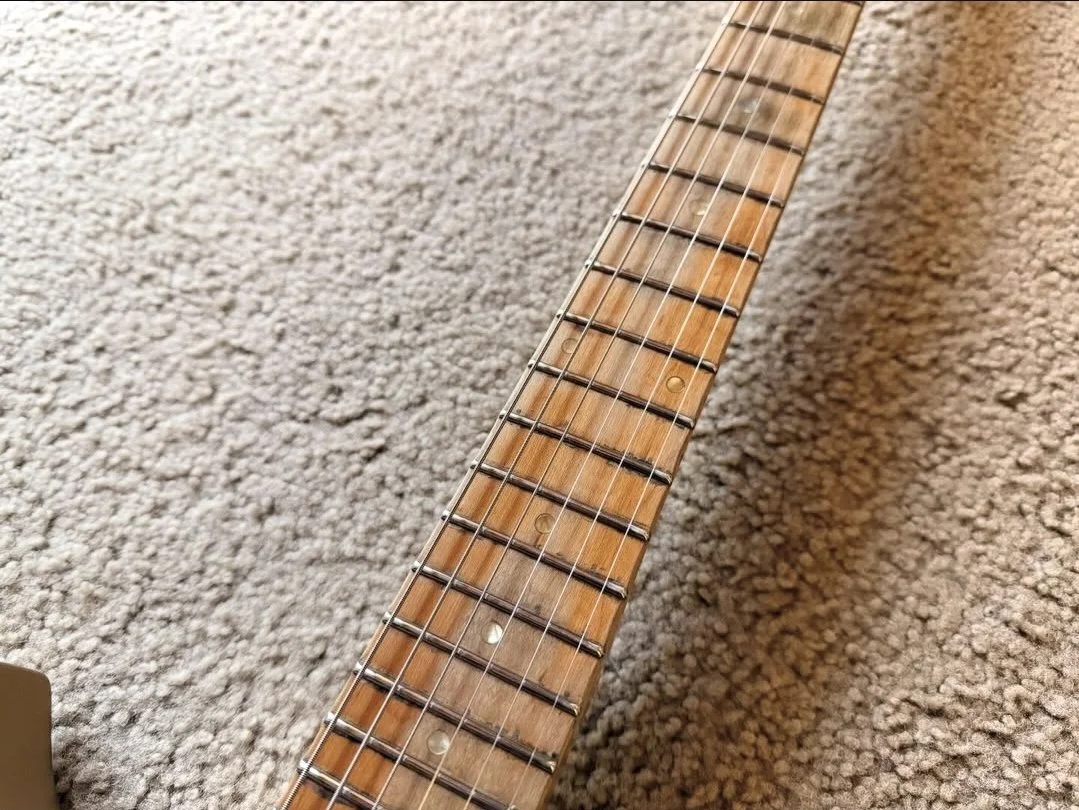 Close-up of a guitar neck with frets and strings on a carpeted floor.