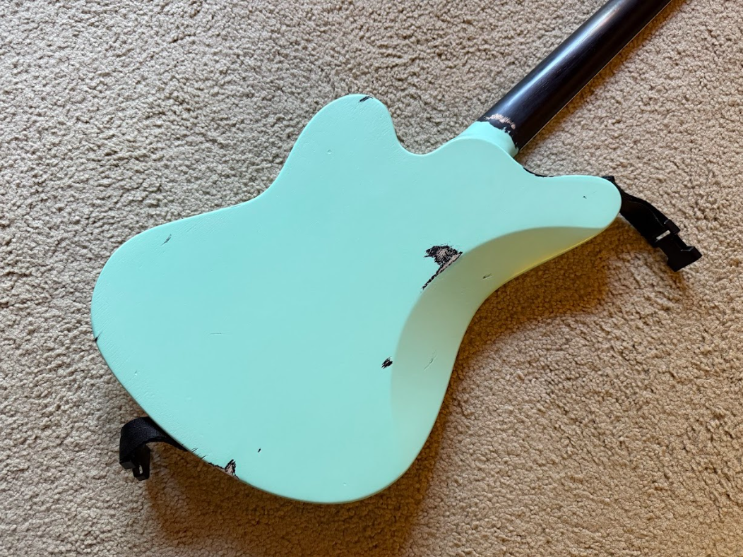 A teal electric guitar body with a black neck resting on a beige carpet, showing some scratches and paint chips.
