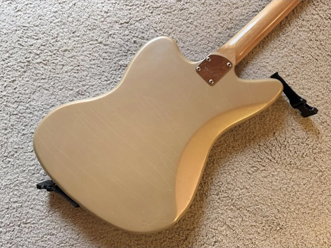 Back of a cream-colored electric guitar lying on a beige carpet.