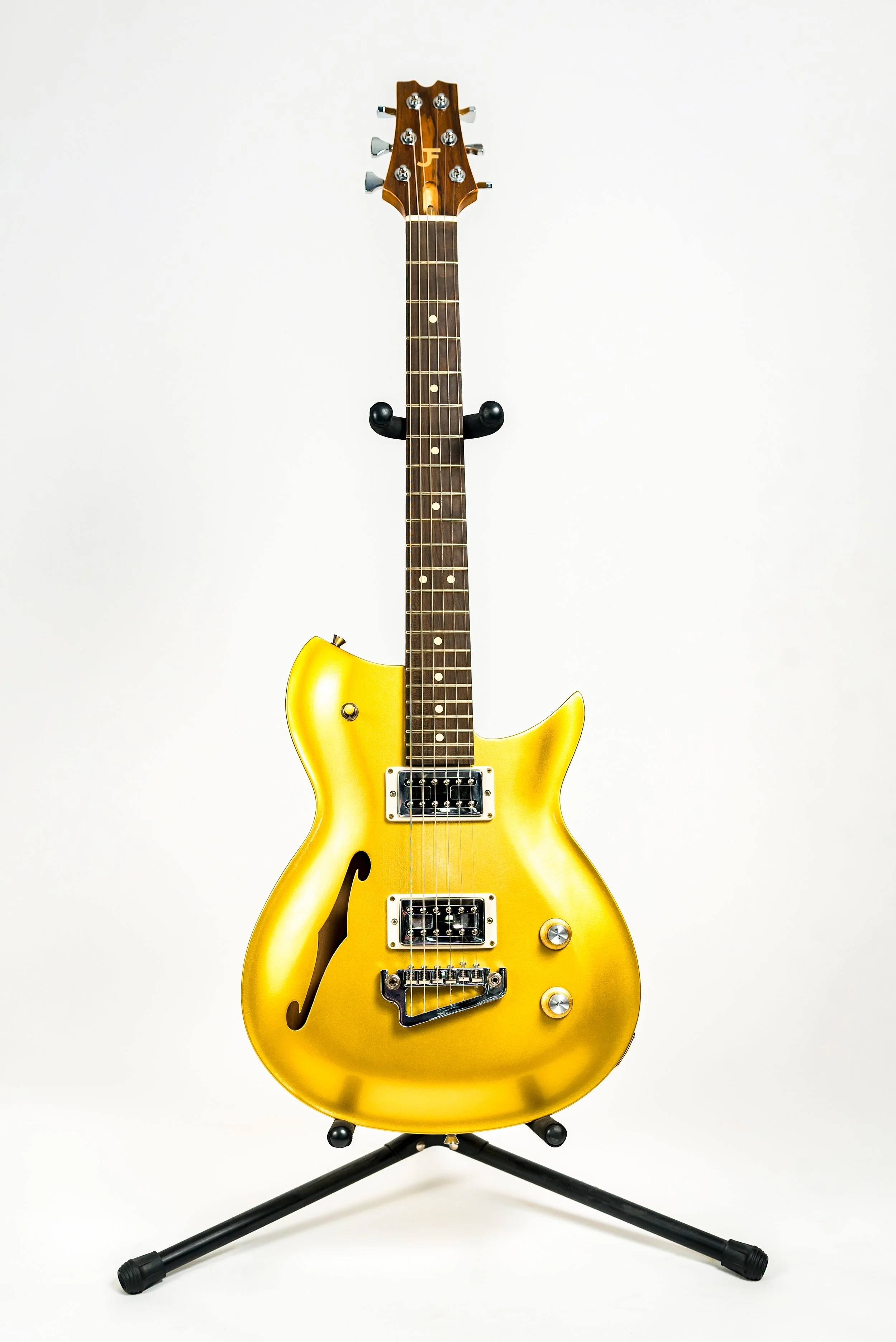 A yellow electric guitar with a semi-hollow body design on a black stand against a white background.
