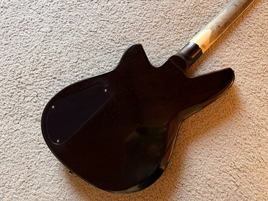 Back of a black electric guitar lying on a beige carpet.