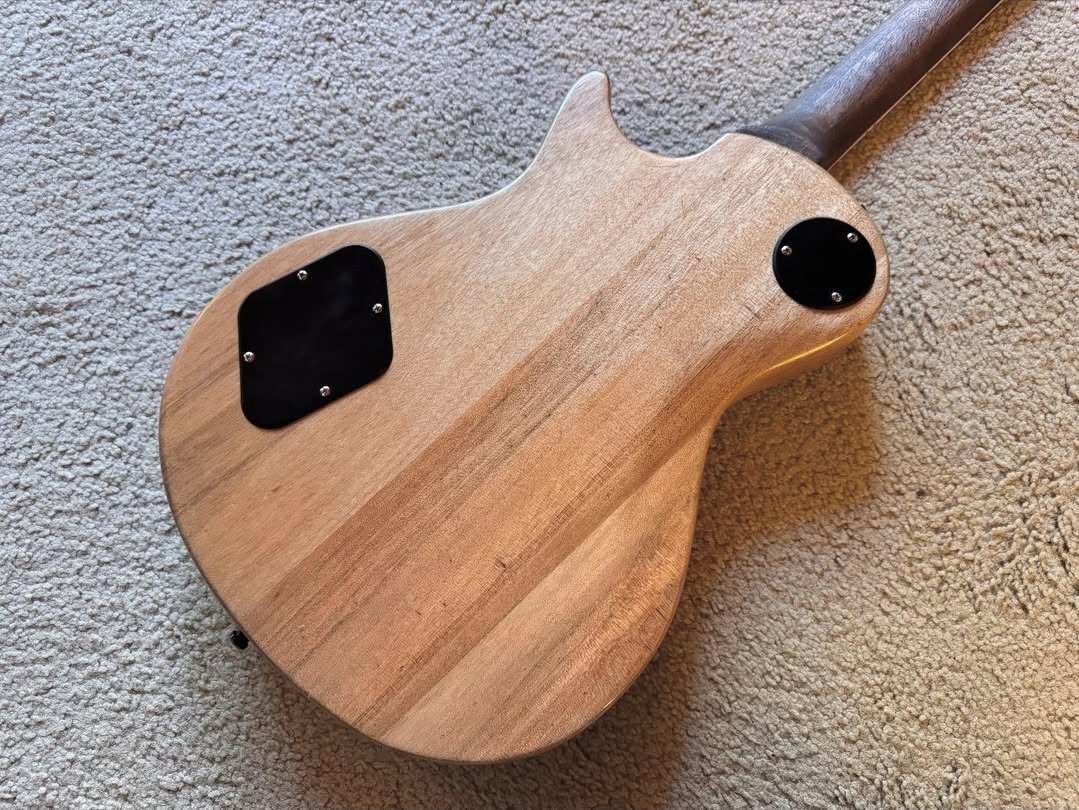 Back of an unfinished electric guitar lying on carpet, showing the wood grain and control cavity covers.