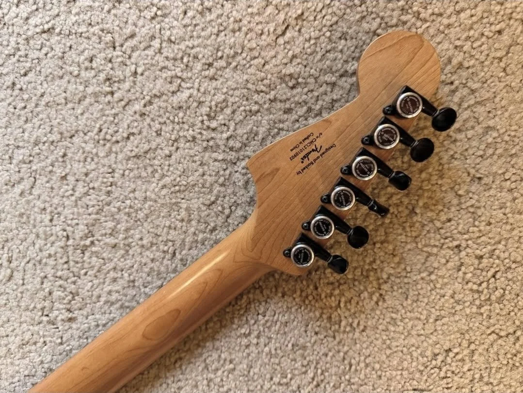 Close-up of the back of a Fender electric guitar headstock with tuning pegs, lying on beige carpet.