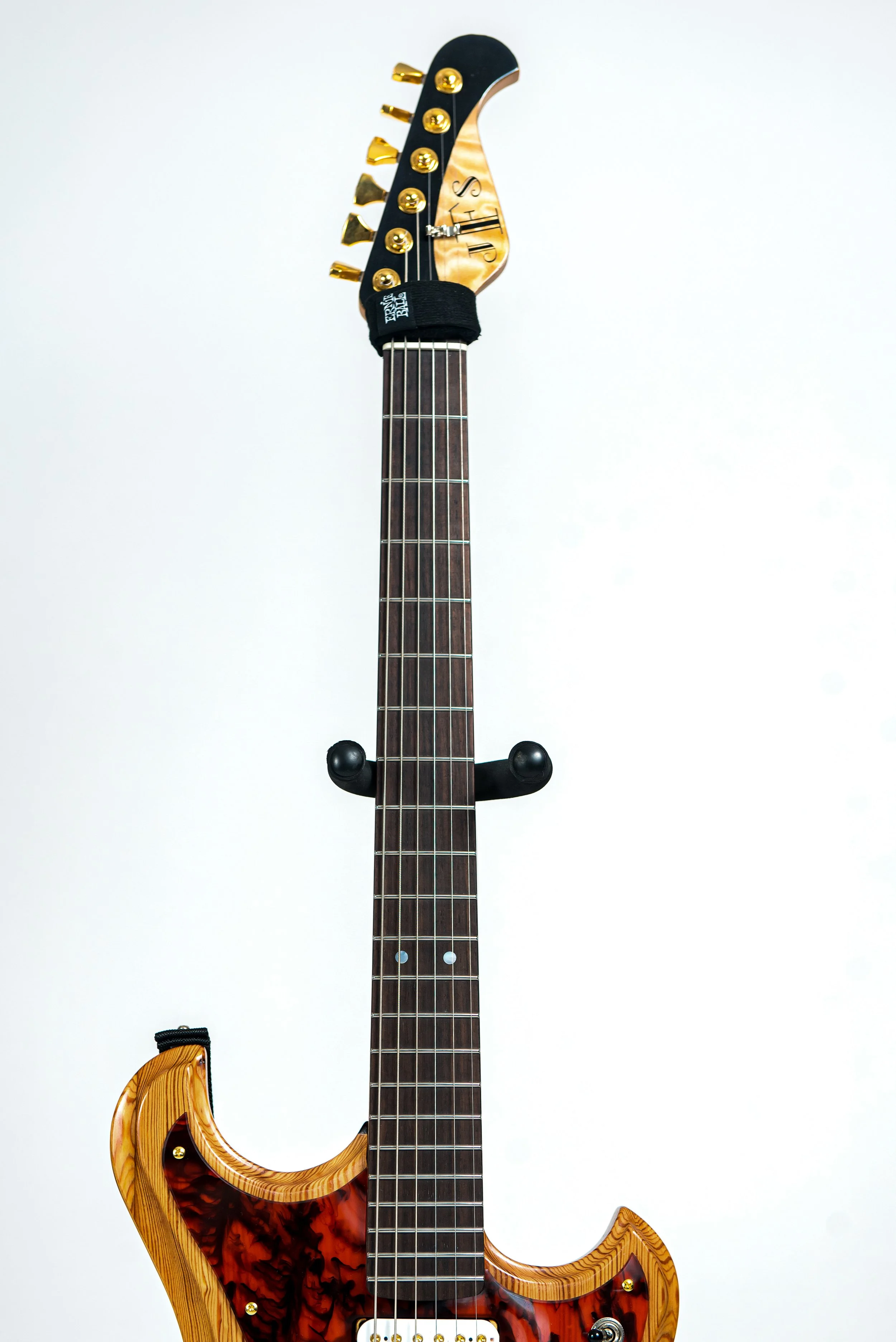 An electric guitar with a wooden body, featuring gold tuning pegs, dark fretboard, and a black strap